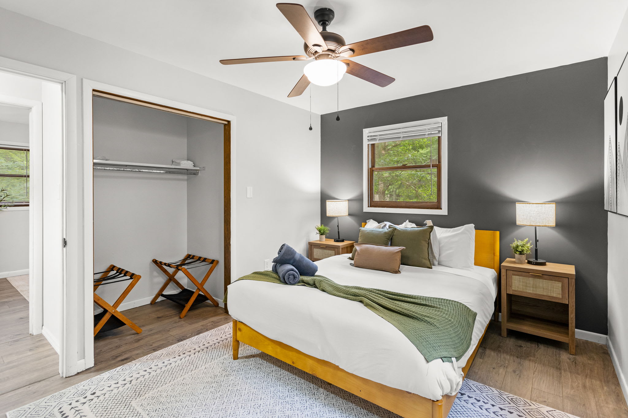 A well-lit bedroom with neatly arranged bedding, a ceiling fan, and an open closet for convenience.