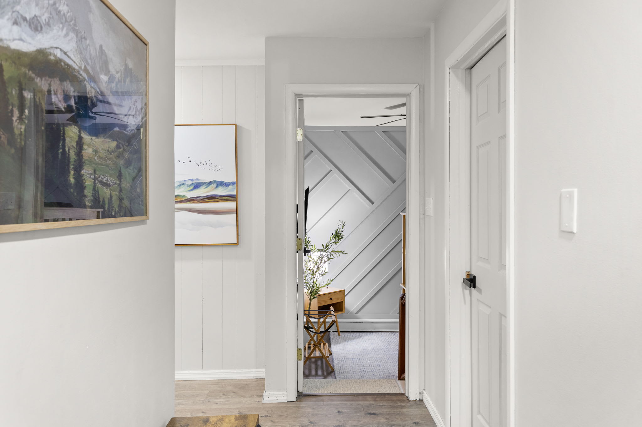 A well-lit hallway leading to additional rooms, with wall art and wooden textures enhancing the aesthetic.