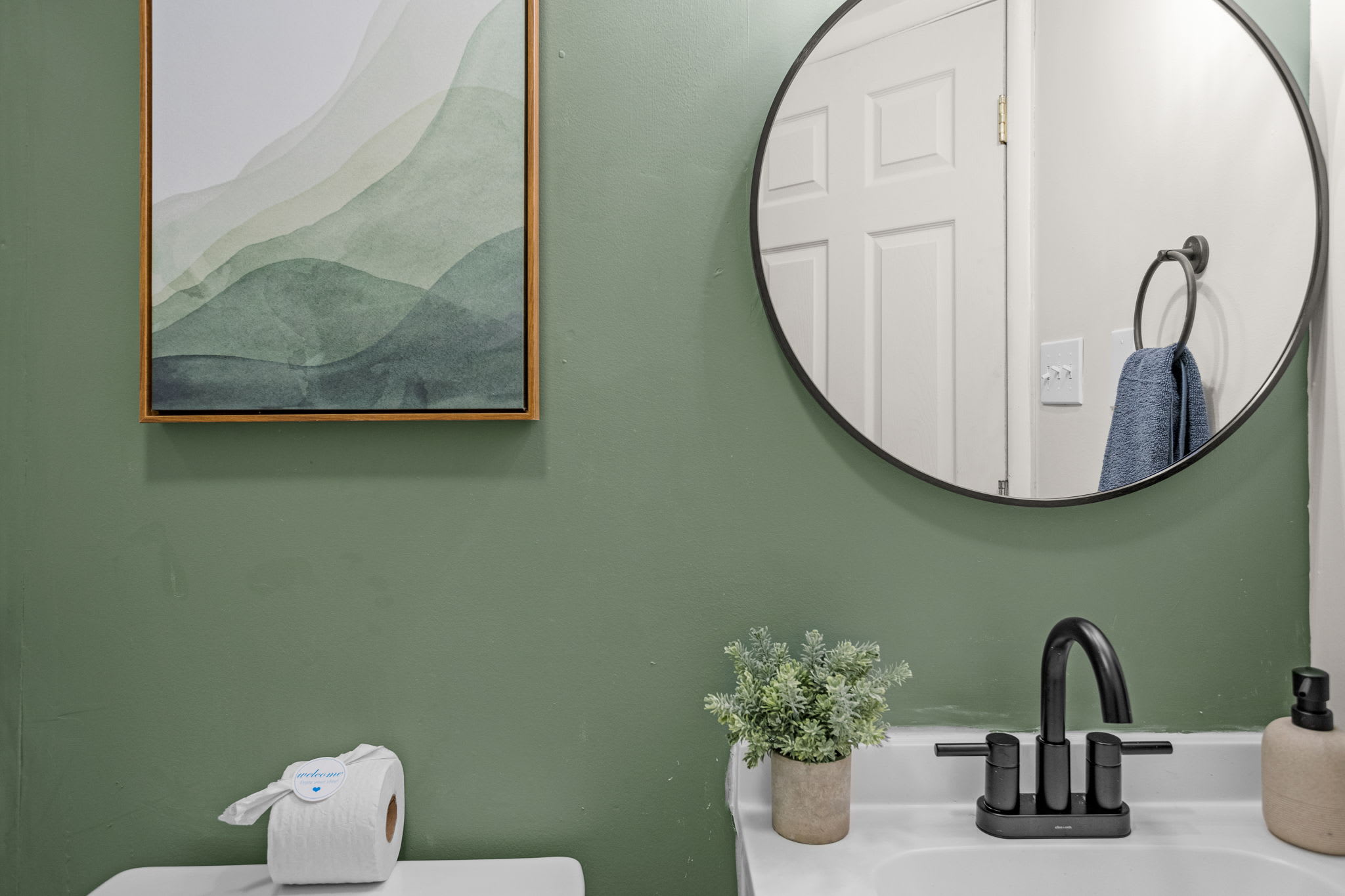 A stylish vanity area with a round mirror, green accent wall, and black faucet details for a modern touch.