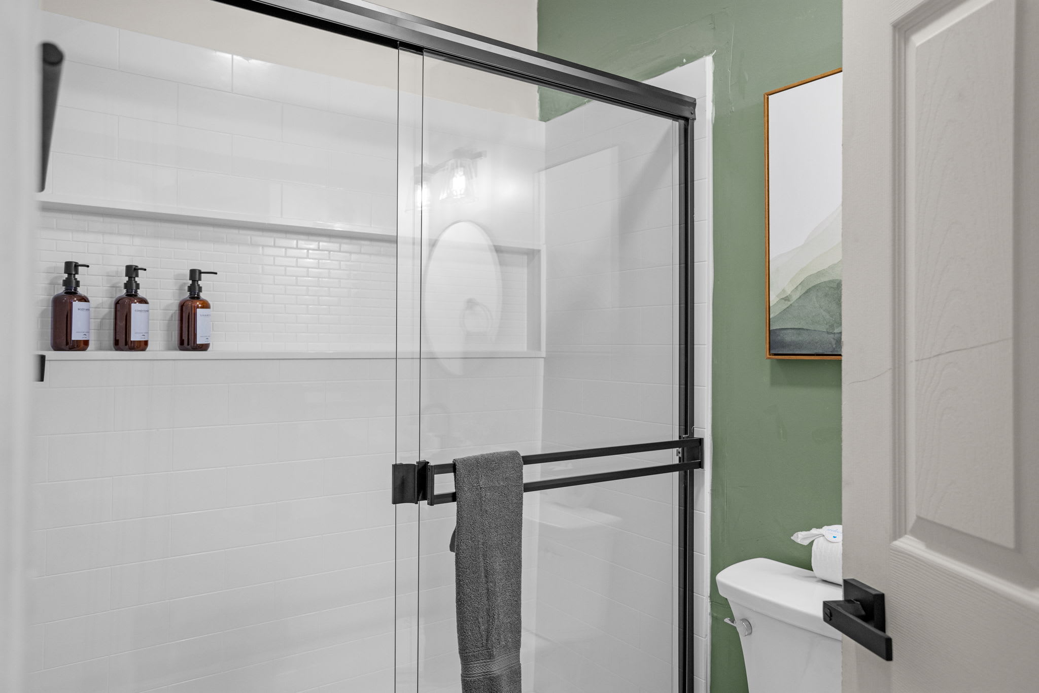 A sleek bathroom with a glass shower enclosure, dark fixtures, and built-in shower dispensers.