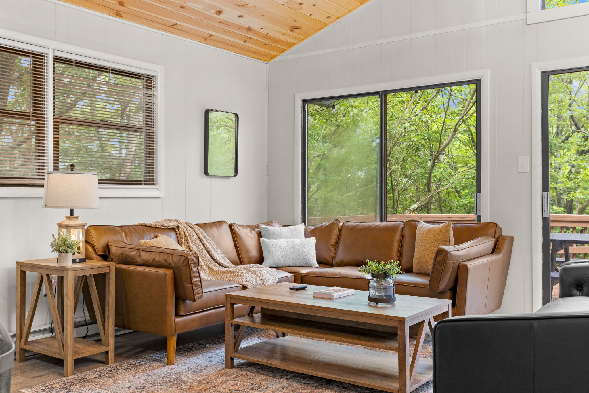A bright and airy living space featuring a leather sectional, large windows, and a warm, inviting ambiance.