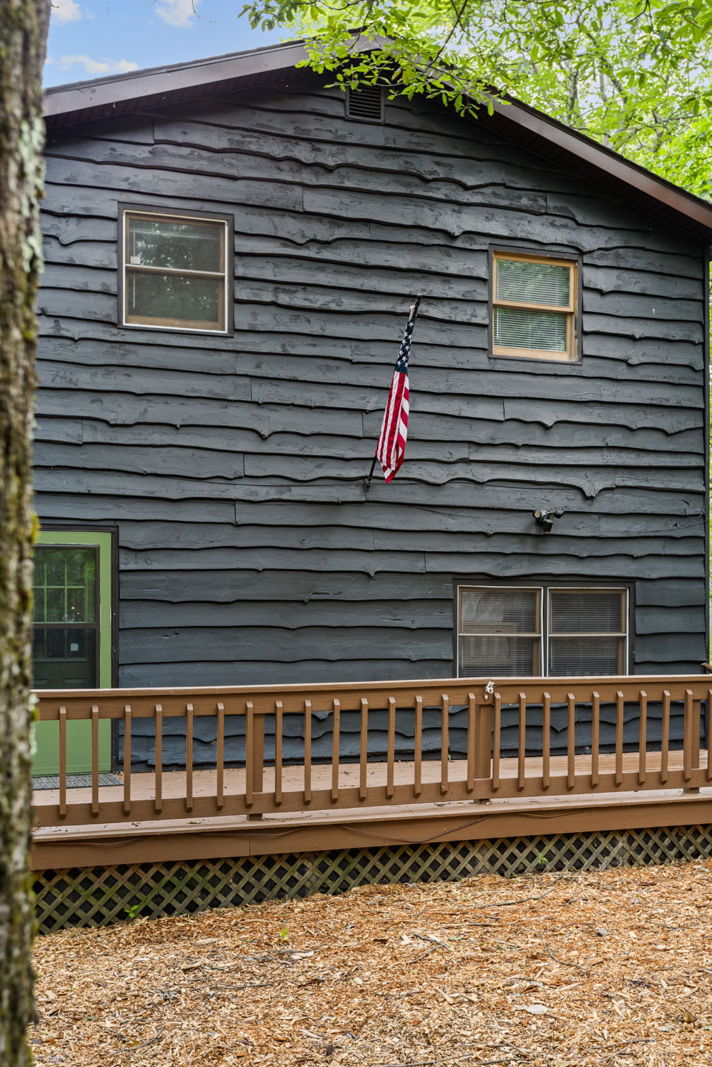 A dark, modern cabin with an American flag, wooden deck, and a charming rustic aesthetic.