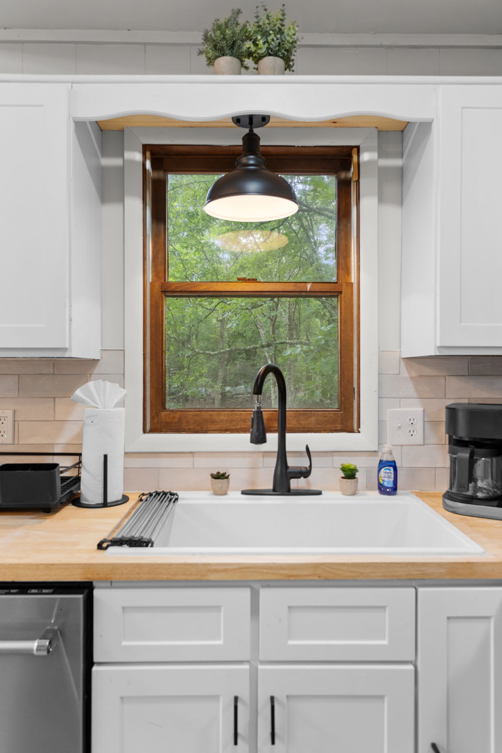 A deep white sink with a black faucet, complemented by a wooden countertop and a small potted plant.