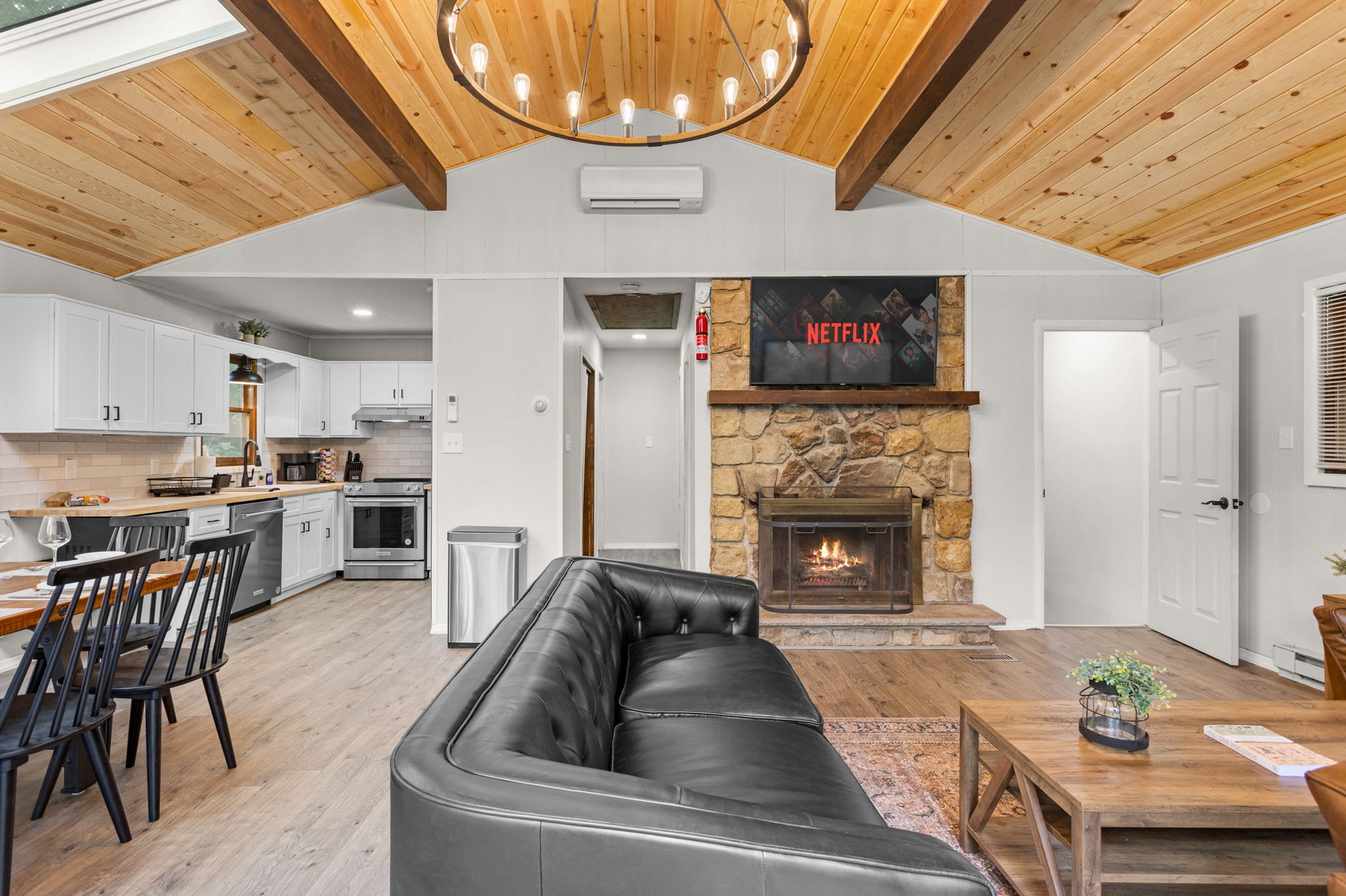Open-Concept Living Space – Vaulted wooden ceilings with a grand chandelier, a stone fireplace, and an elegant dining setup create a warm and inviting atmosphere.