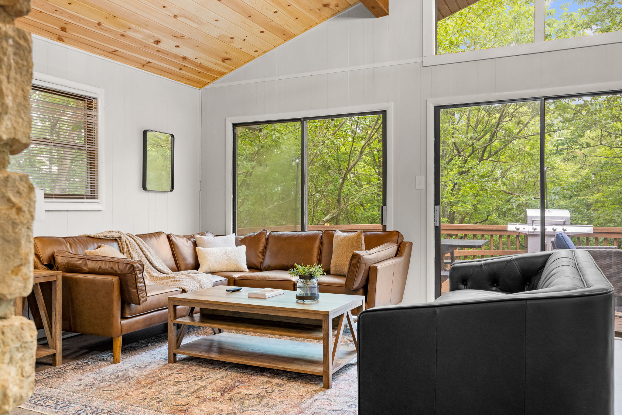 The vaulted ceilings with skylights, stone fireplace, and large leather seating create an inviting atmosphere. Floor-to-ceiling windows bring in an abundance of natural light and offer serene forest views.