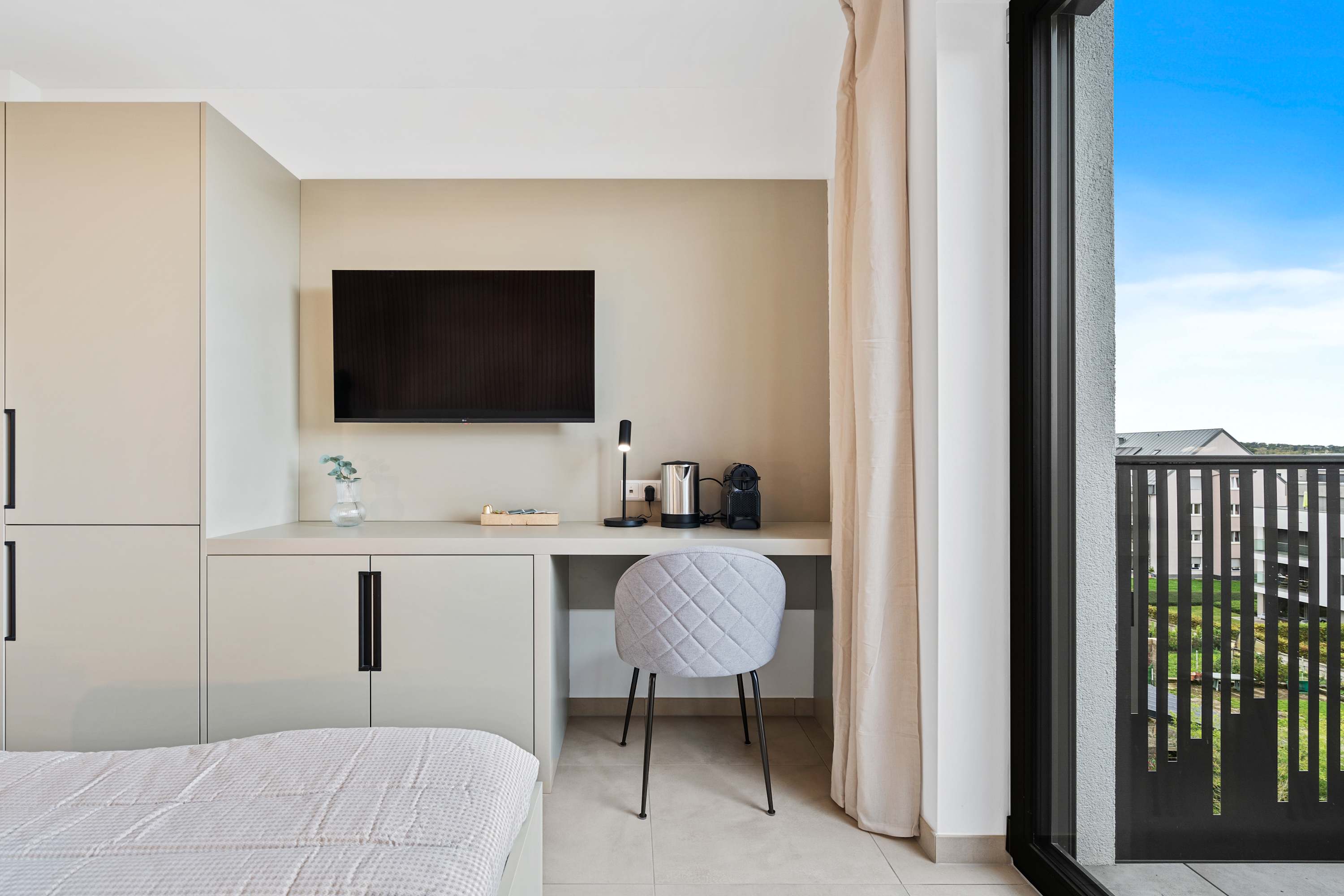 Functional Workspace and Entertainment Area – Wall-mounted TV, small desk, and a cozy chair create a perfect blend of comfort and productivity.