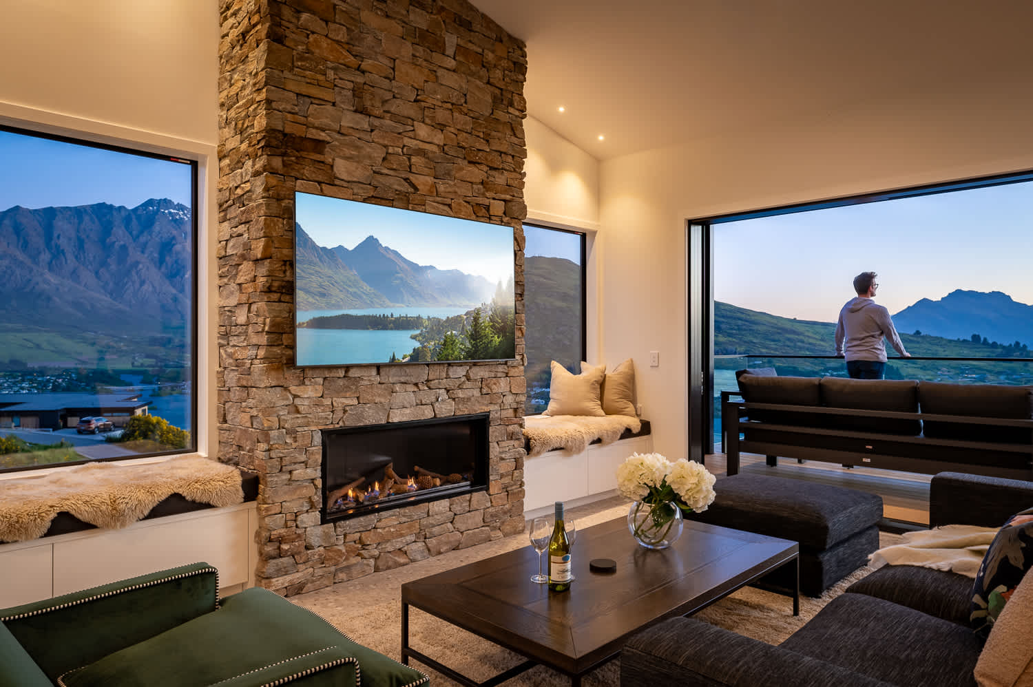 Unwind in a cozy living room with a warm fireplace, offering stunning views of Lake Wakatipu and the surrounding mountains