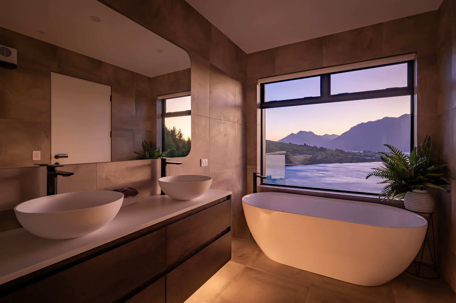 Relax in a beautifully designed indoor bathtub with floor-to-ceiling windows offering a panoramic view of Lake Wakatipu and the surrounding mountains.