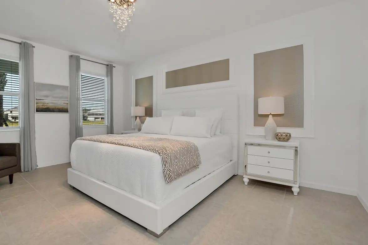 Relax in this elegant bedroom featuring a plush bed, chic chandelier, and ample natural light for a serene retreat.
