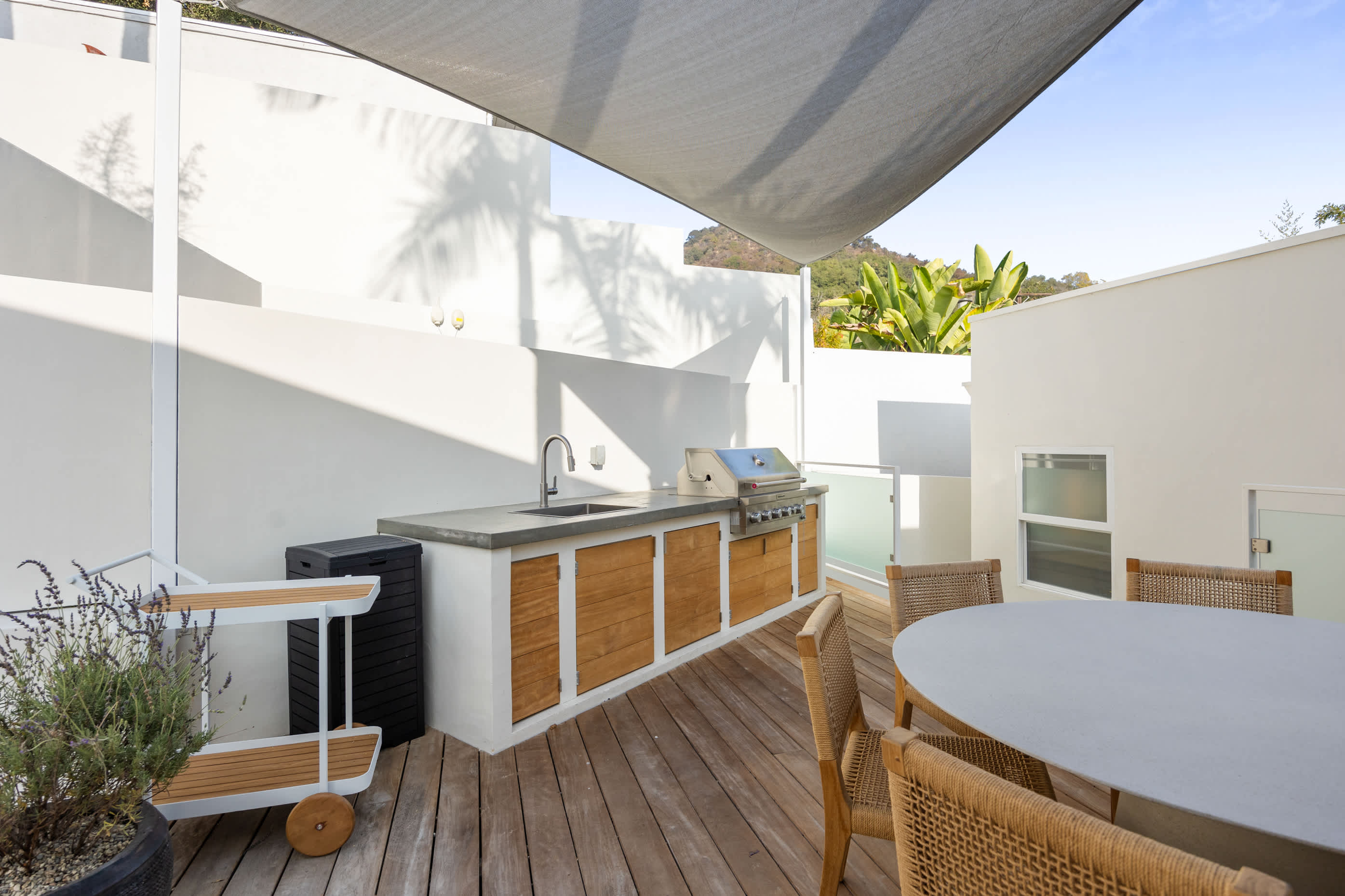 Outdoor kitchen with sleek wood-panel cabinetry, built-in grill, and shaded design elements.