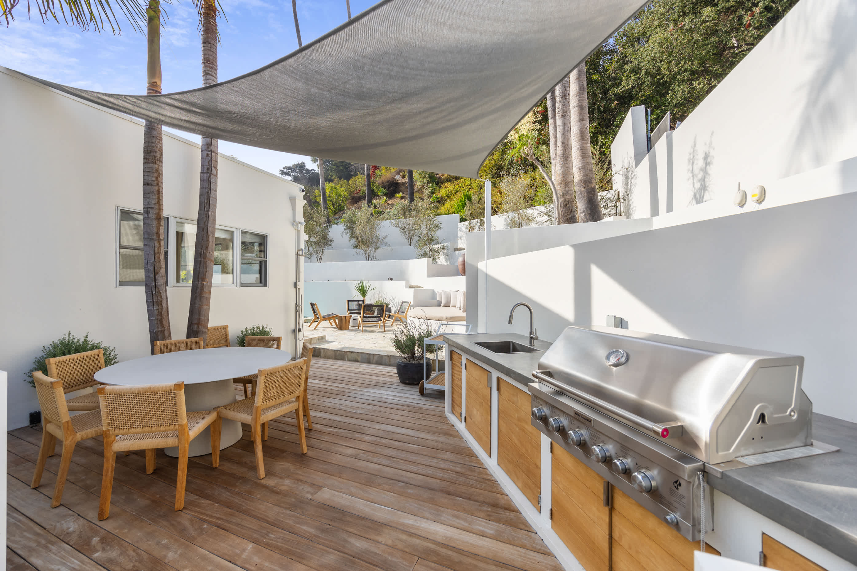 Expansive BBQ area with polished finishes, decked flooring, and a lush backdrop.