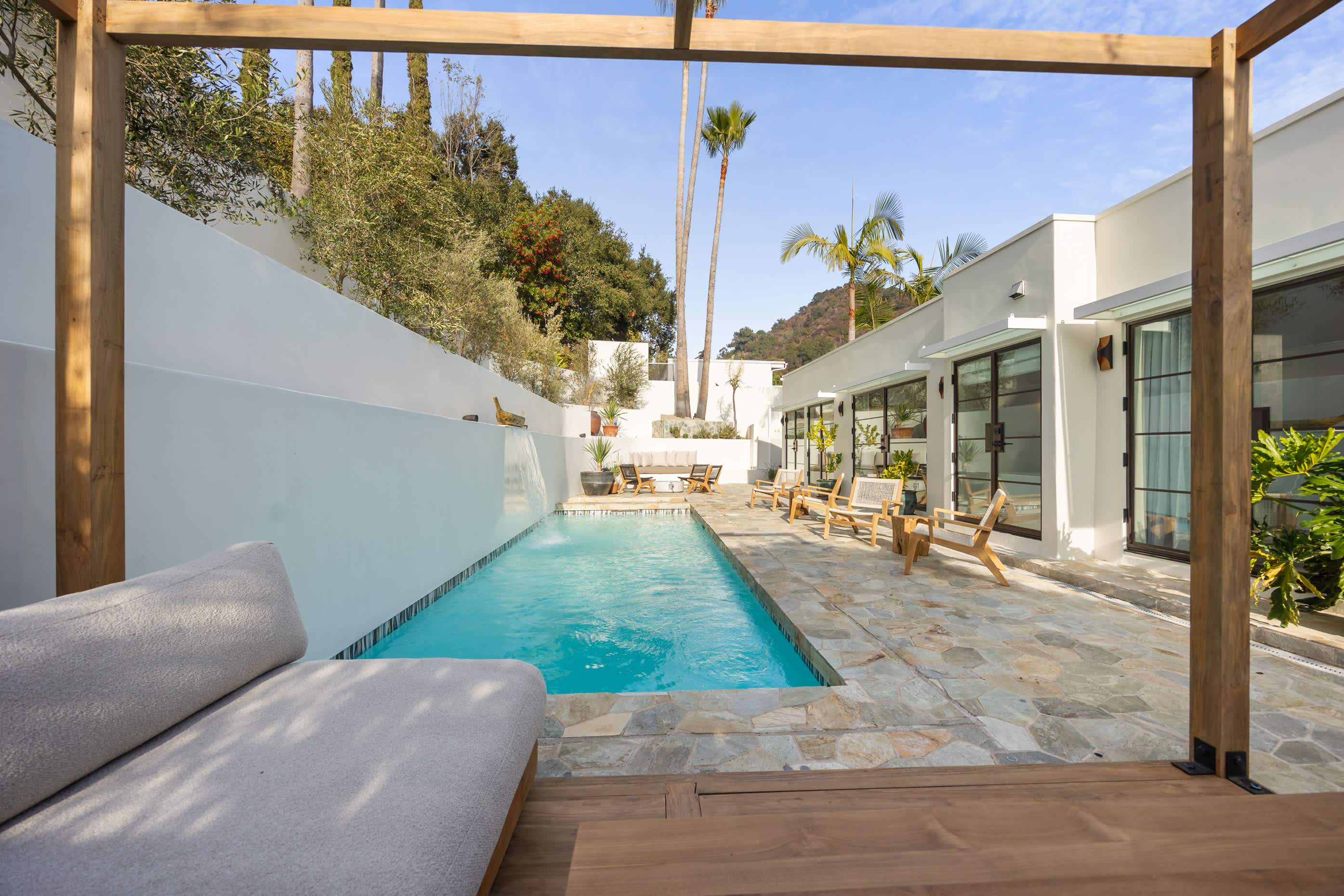 The expansive pool stretches under open skies, framed by lush greenery and modern lines.