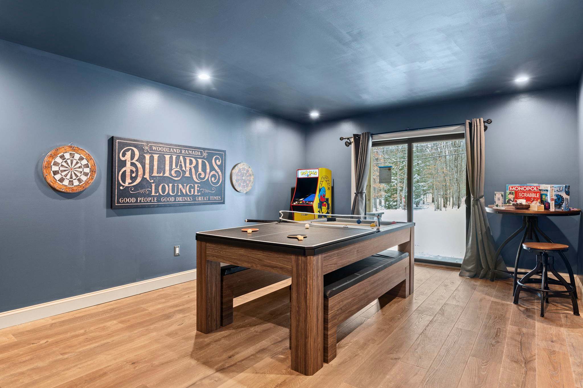 The game room features a custom billiards table, dart boards, and a retro arcade, perfect for friendly competition amid a stylish navy-blue setting.