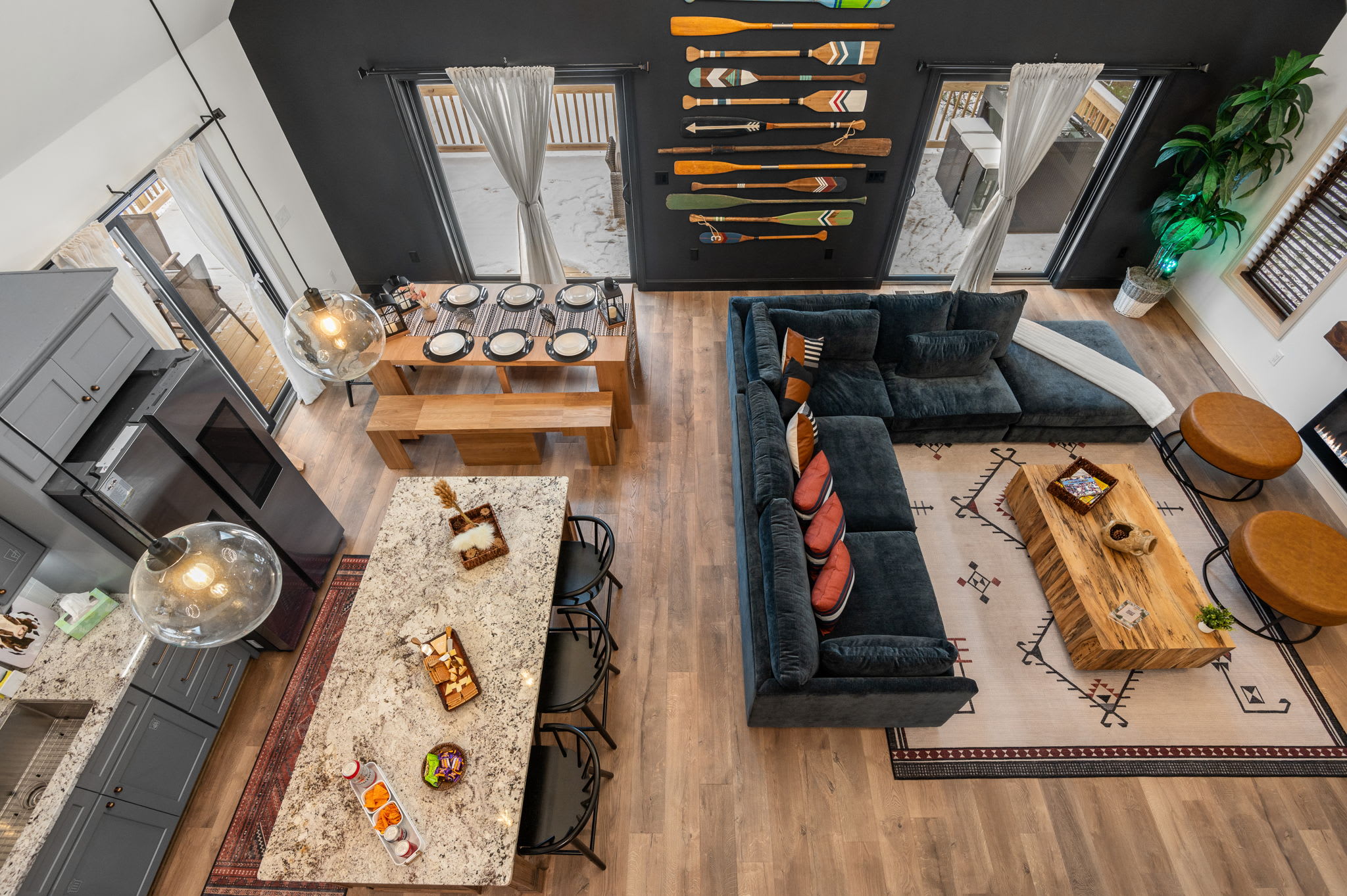 An open-concept living space unites the kitchen, dining, and lounge areas. Rustic paddles on a black accent wall and a plush sectional create a chic, cabin-inspired vibe.