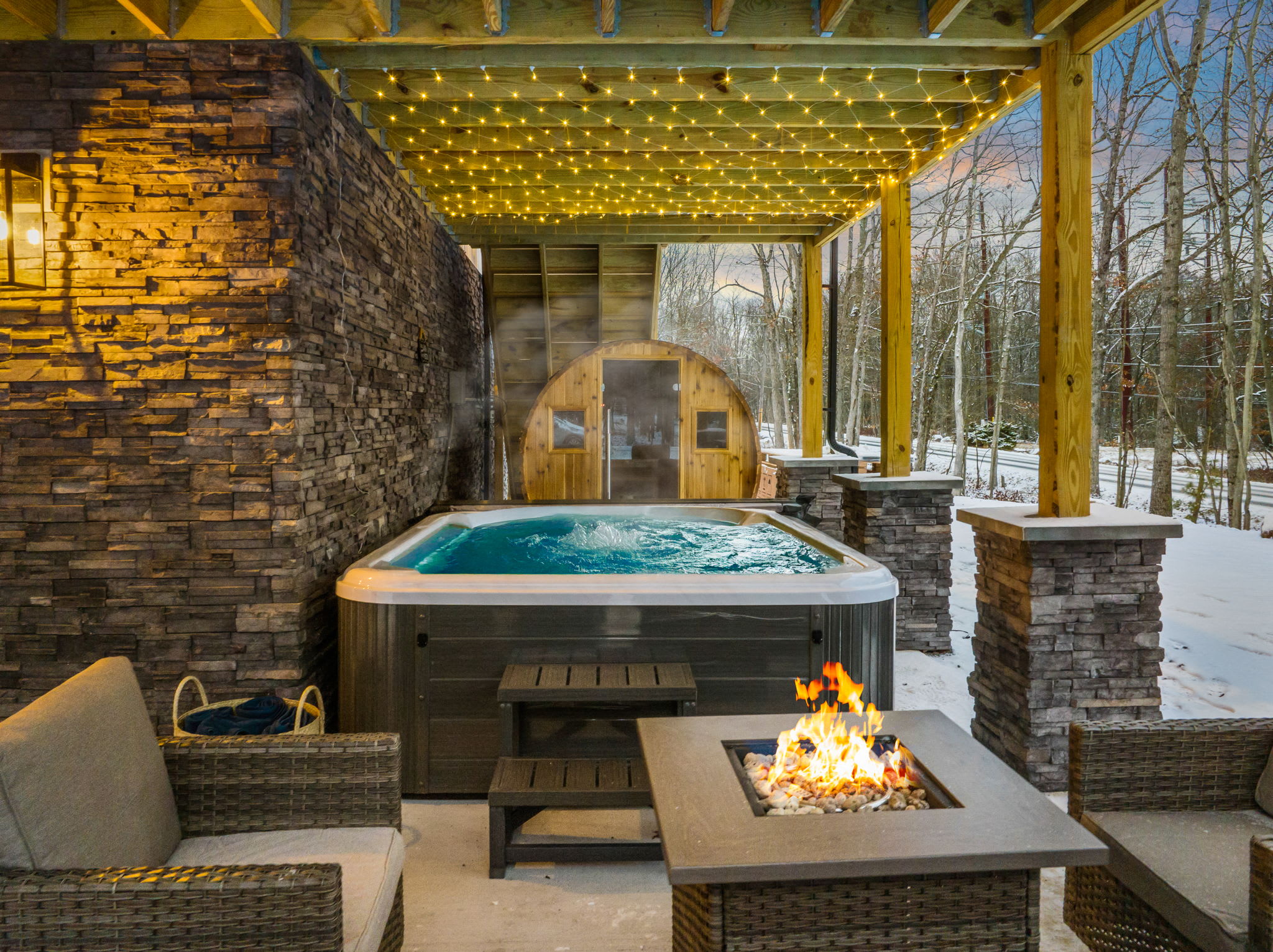 Under twinkling lights, the hot tub area invite you to cozy up, while a barrel sauna in the background promises a soothing, spa-like escape.