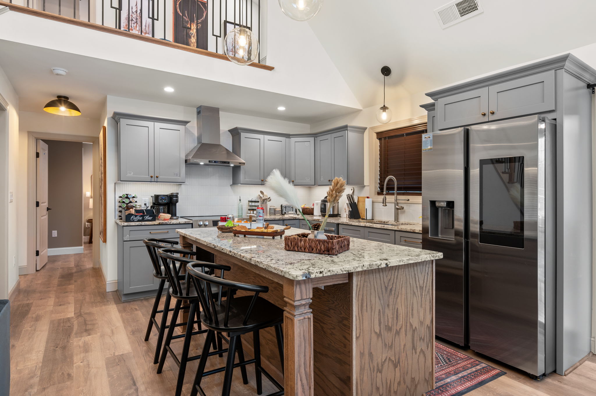The kitchen’s gray cabinetry, granite island, and stainless steel appliances blend style and function, creating a welcoming hub for shared meals and conversation.