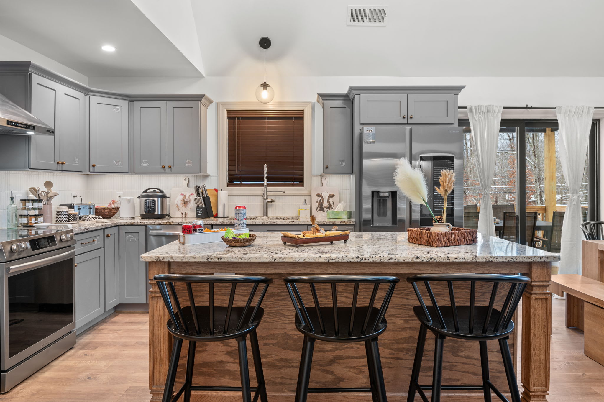 The open kitchen layout features gray cabinetry, a roomy granite island, and bar seating, perfect for gathering around and chatting.