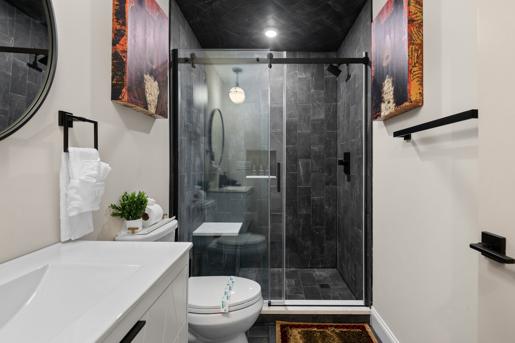 This contemporary bathroom features striking dark tiles, elegant lighting, and a glass shower with a built-in bench, an upscale retreat to refresh and recharge.