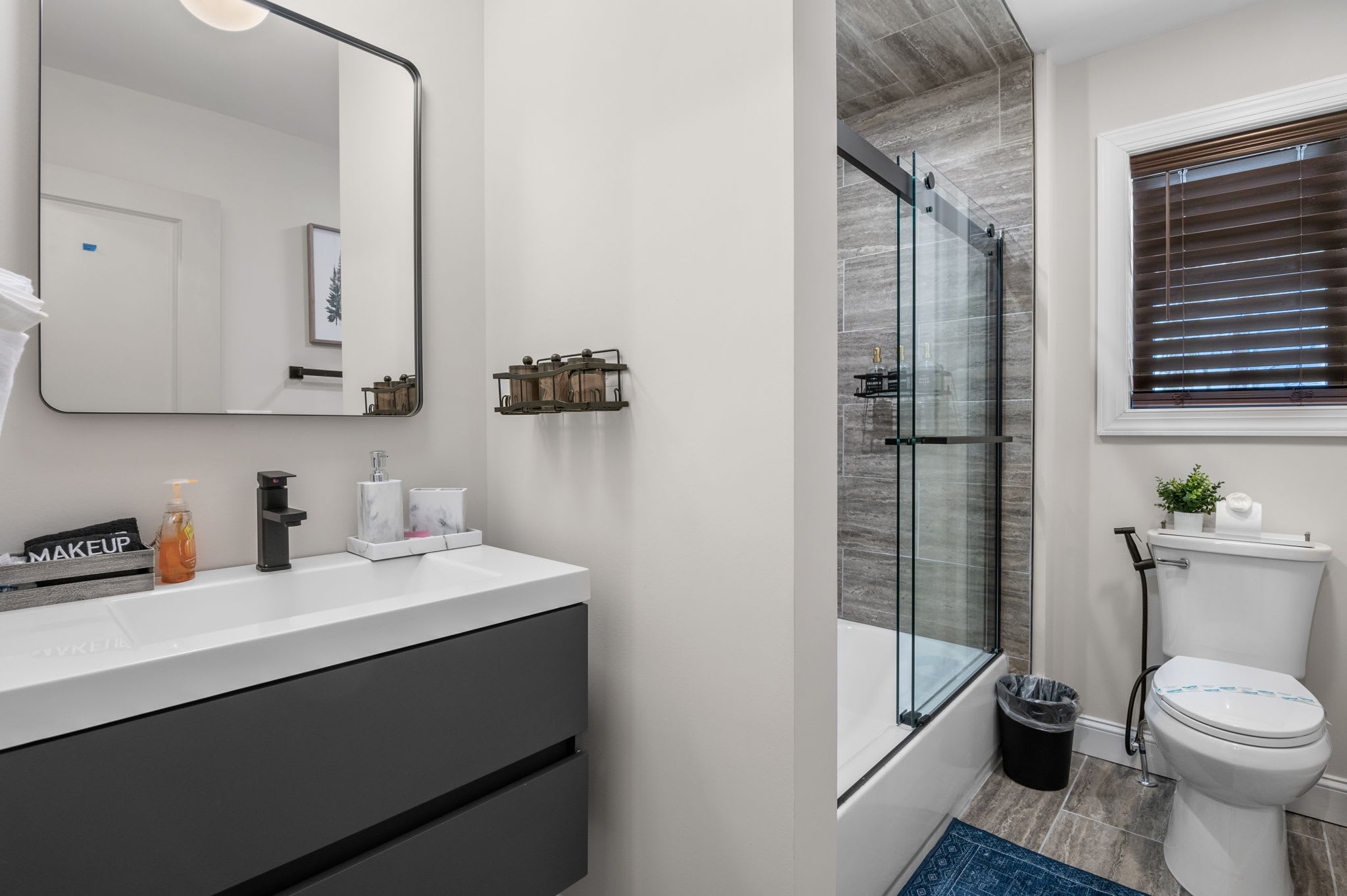 Clean, minimal, and inviting, this modern bathroom offers a spacious vanity, a well-lit mirror, and a cozy tub/shower combination for ultimate convenience.