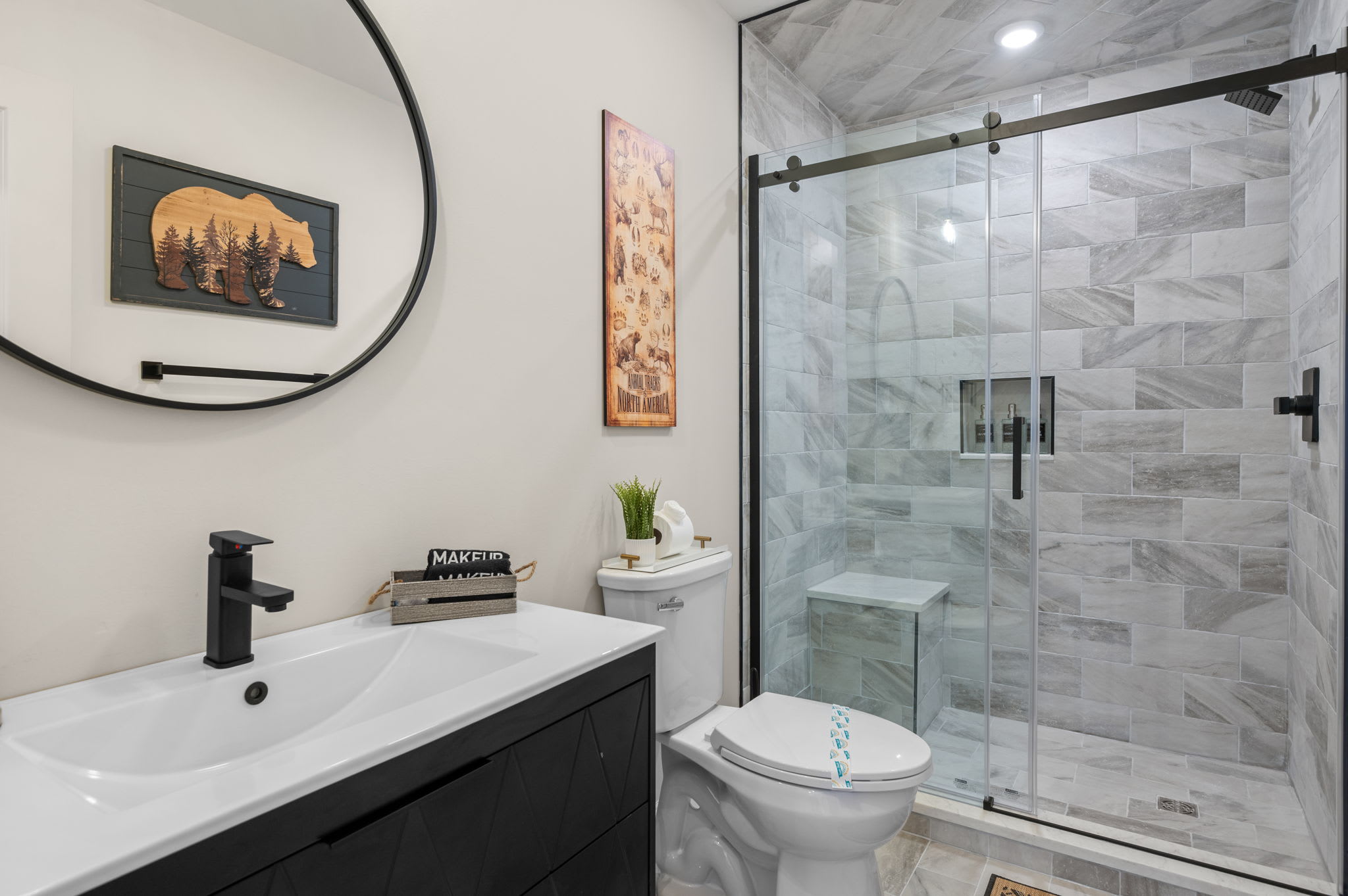 A cozy, cabin-inspired bathroom with woodsy decor, warm lighting, and a glass walk-in shower, blending relaxation and style.