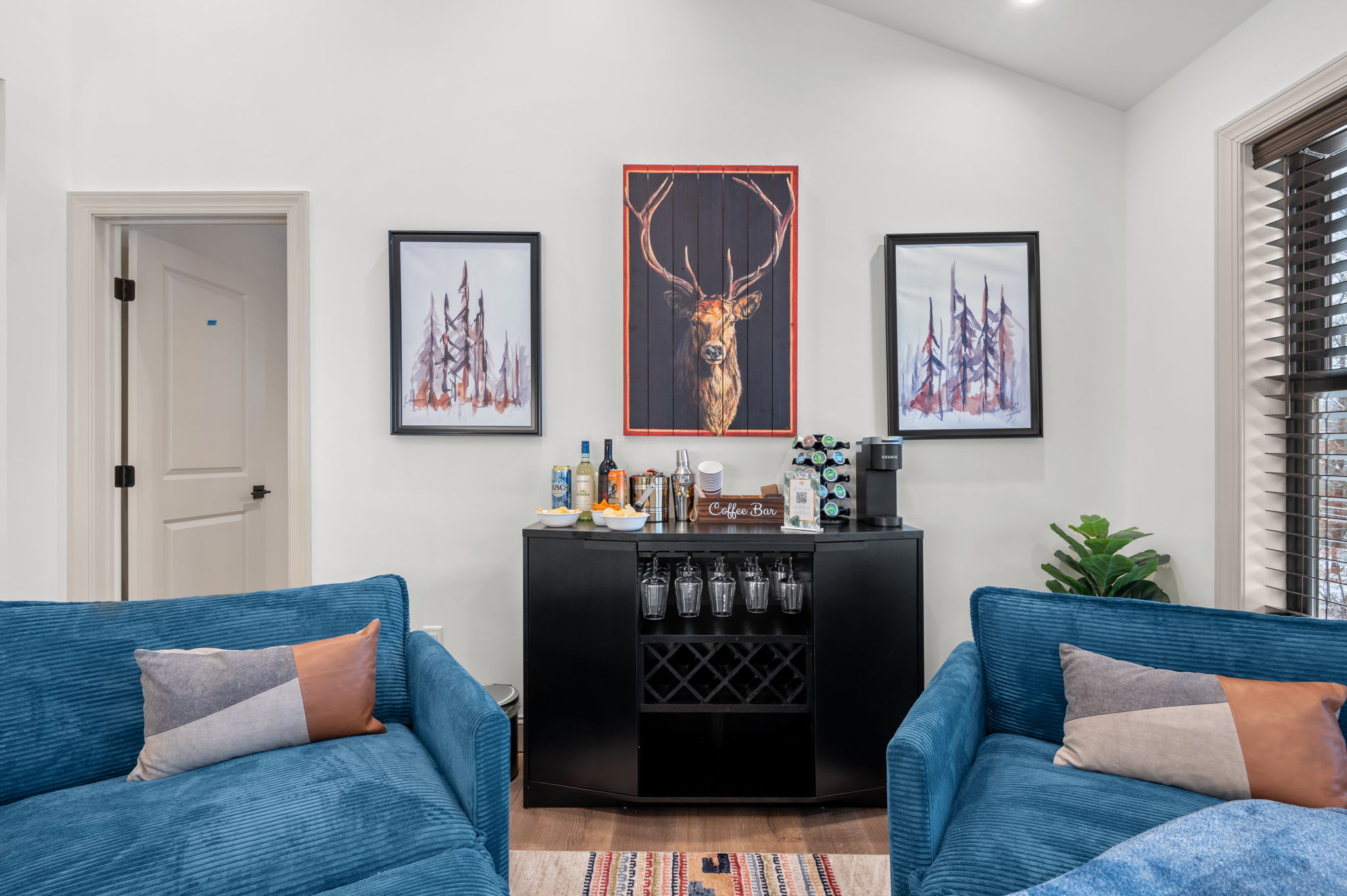 A cozy lounge corner features plush blue chairs and a sleek bar, framed by nature-themed artwork, a perfect spot to sip and relax.