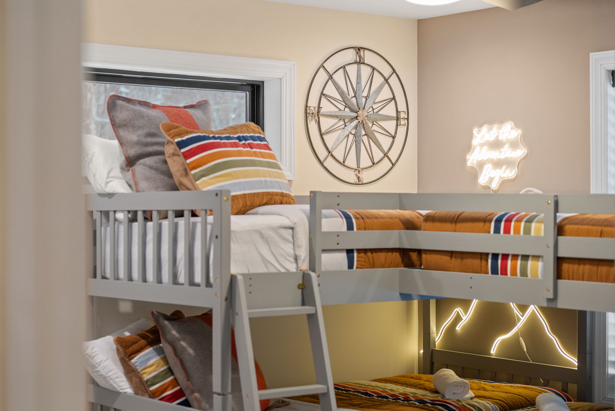 In the bunk room, striped bedding, a compass clock, and a playful neon sign bring an adventurous, kid-friendly spirit.