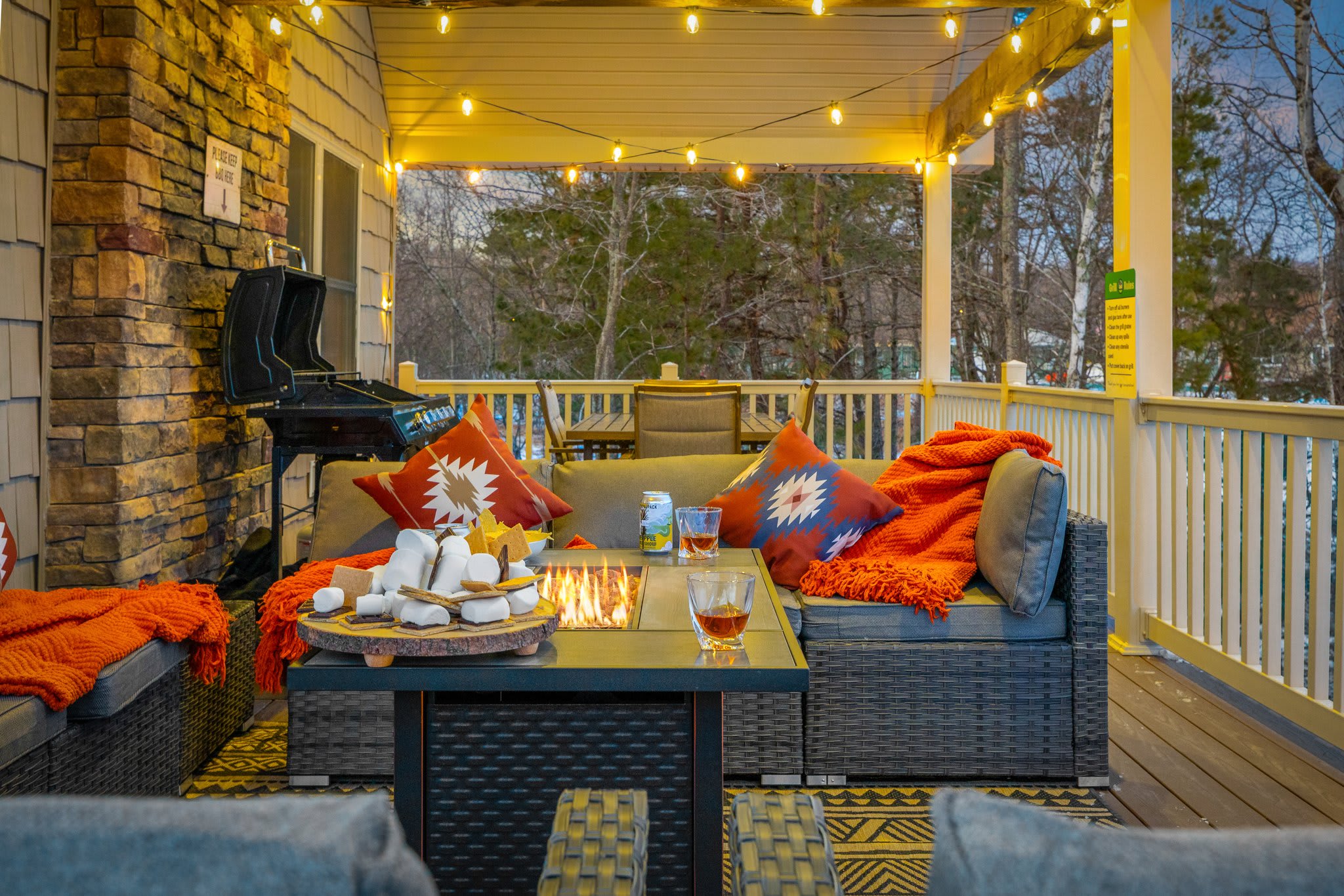 Cozy lounge setup with string lights overhead, a fire table in the center, and warm throws ready for chilly evenings.