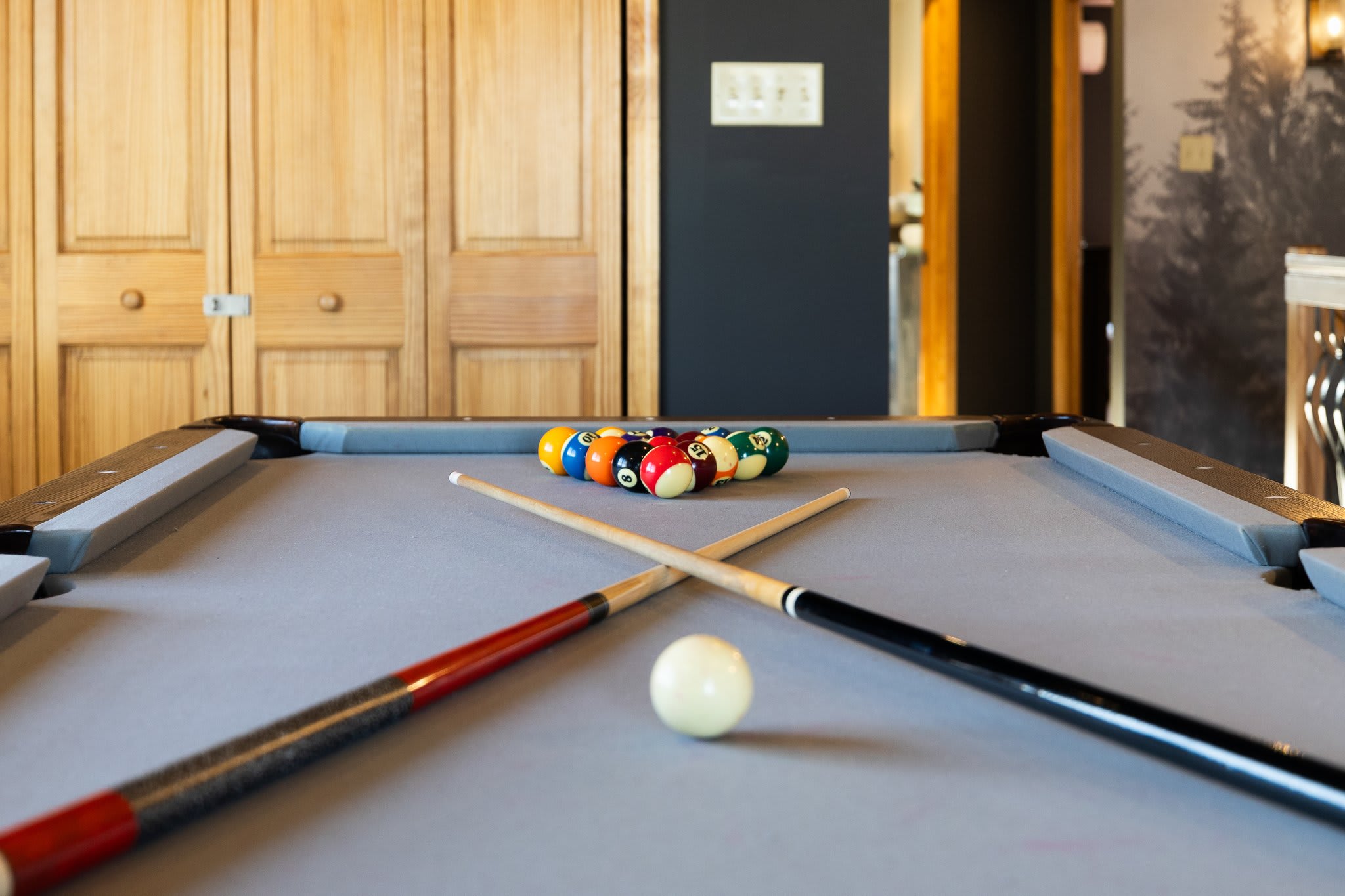 A clean shot of the pool table, cues lined up and ready beneath warm wood cabinetry.
