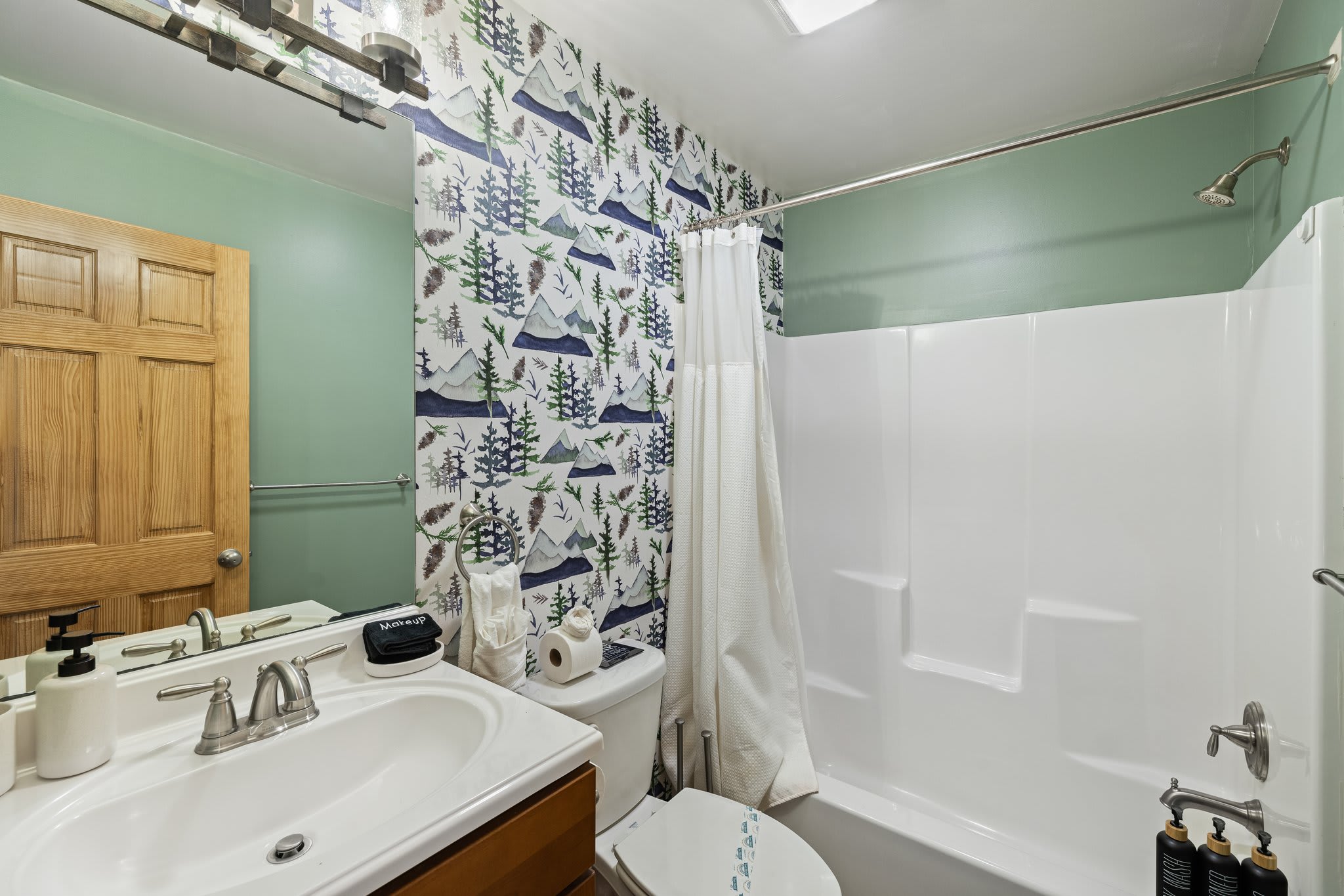 A forest-themed shower curtain and light wood vanity give this bathroom a cozy, outdoorsy charm.