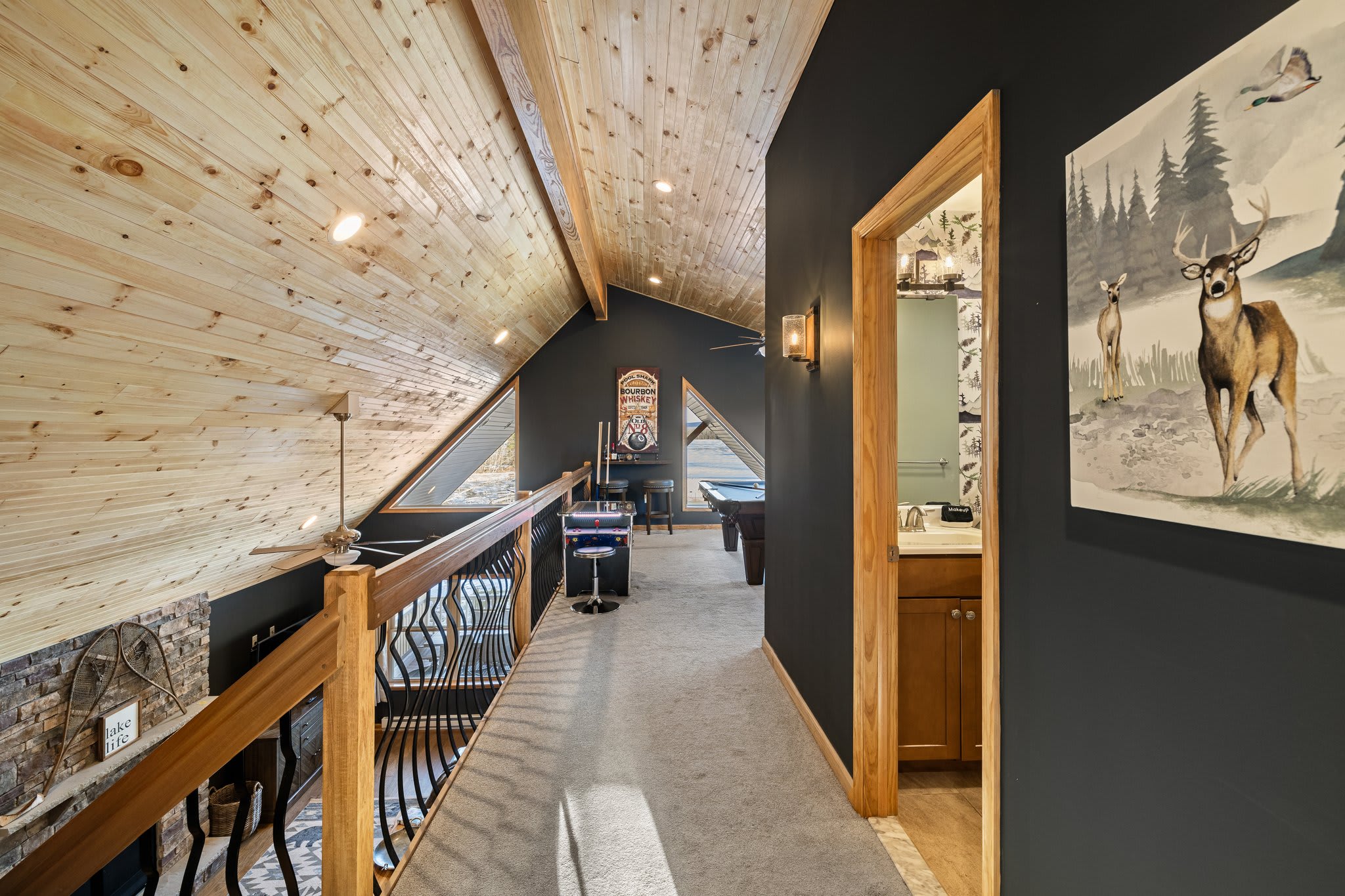 A scenic upstairs hallway framed by sloped wooden ceilings and forest-inspired art. Leads to the perfect retreat.