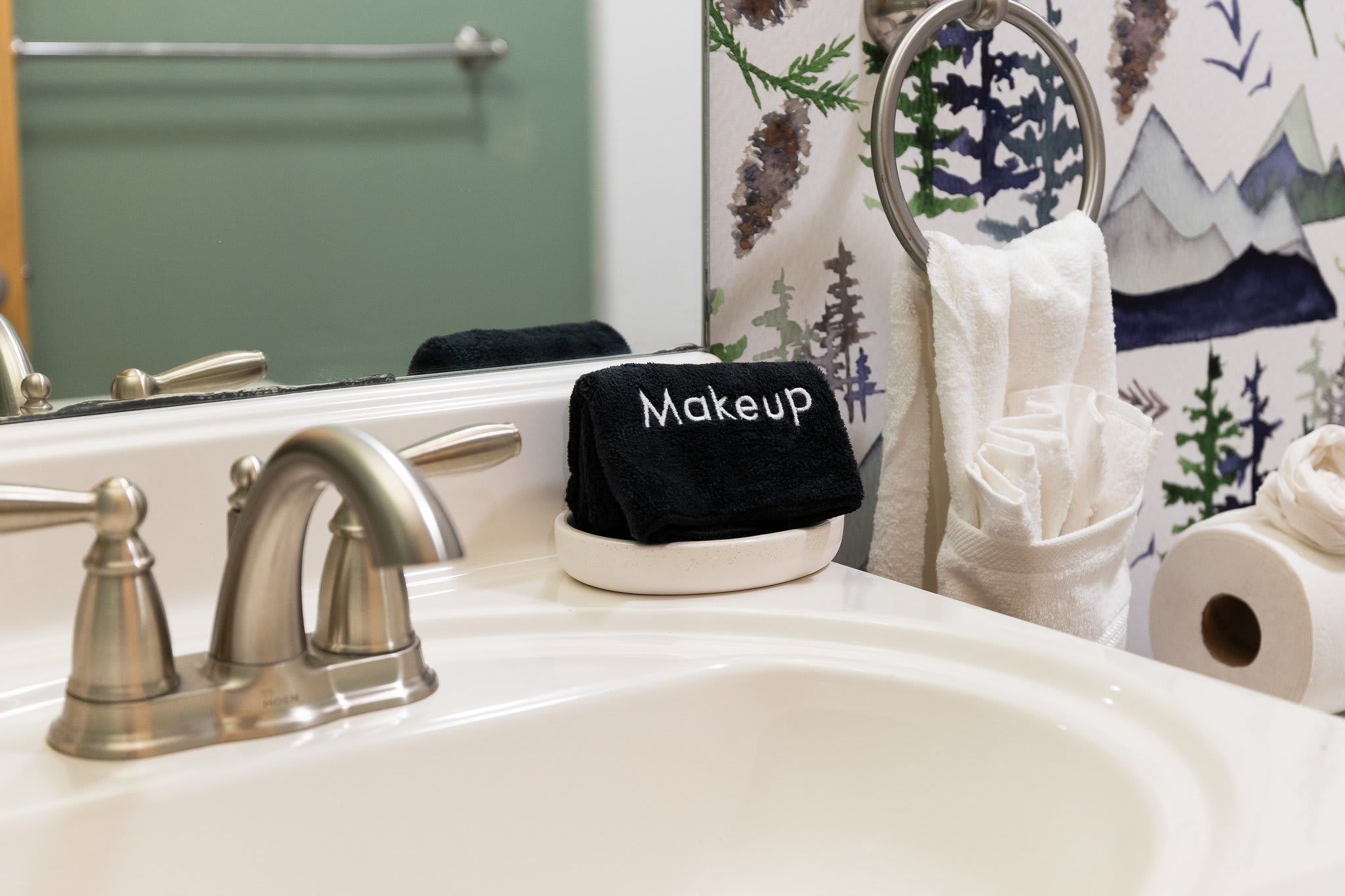 A neatly staged sink with forest-print wallpaper and a cute black “Makeup” towel, it’s giving peaceful morning routines.