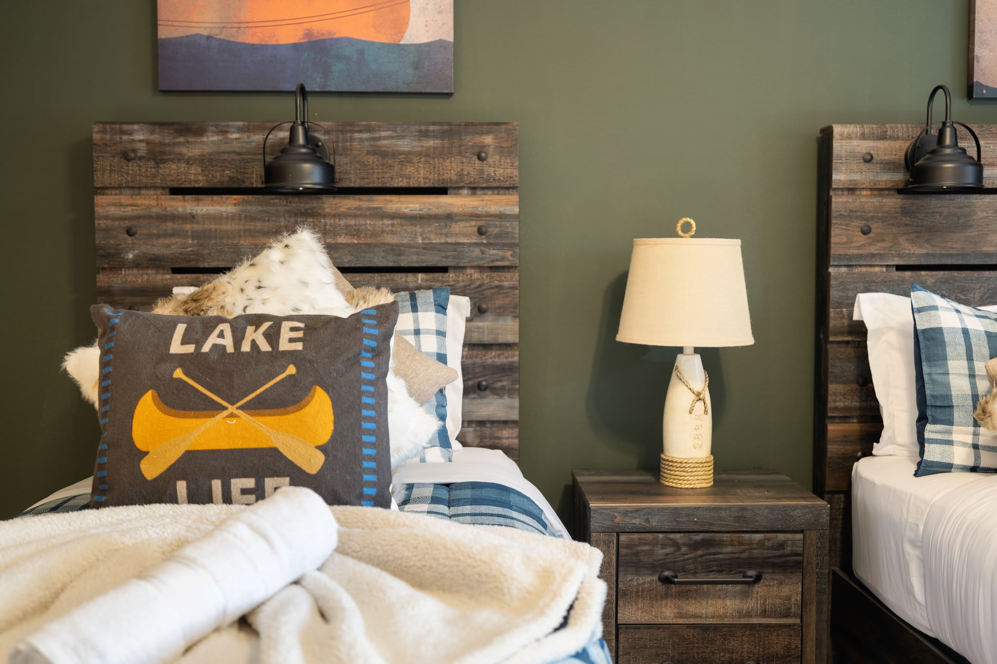 Beds with rustic wood headboards, plaid pillows, and a cute “Lake Life” accent give this space a cozy, nature-loving charm.