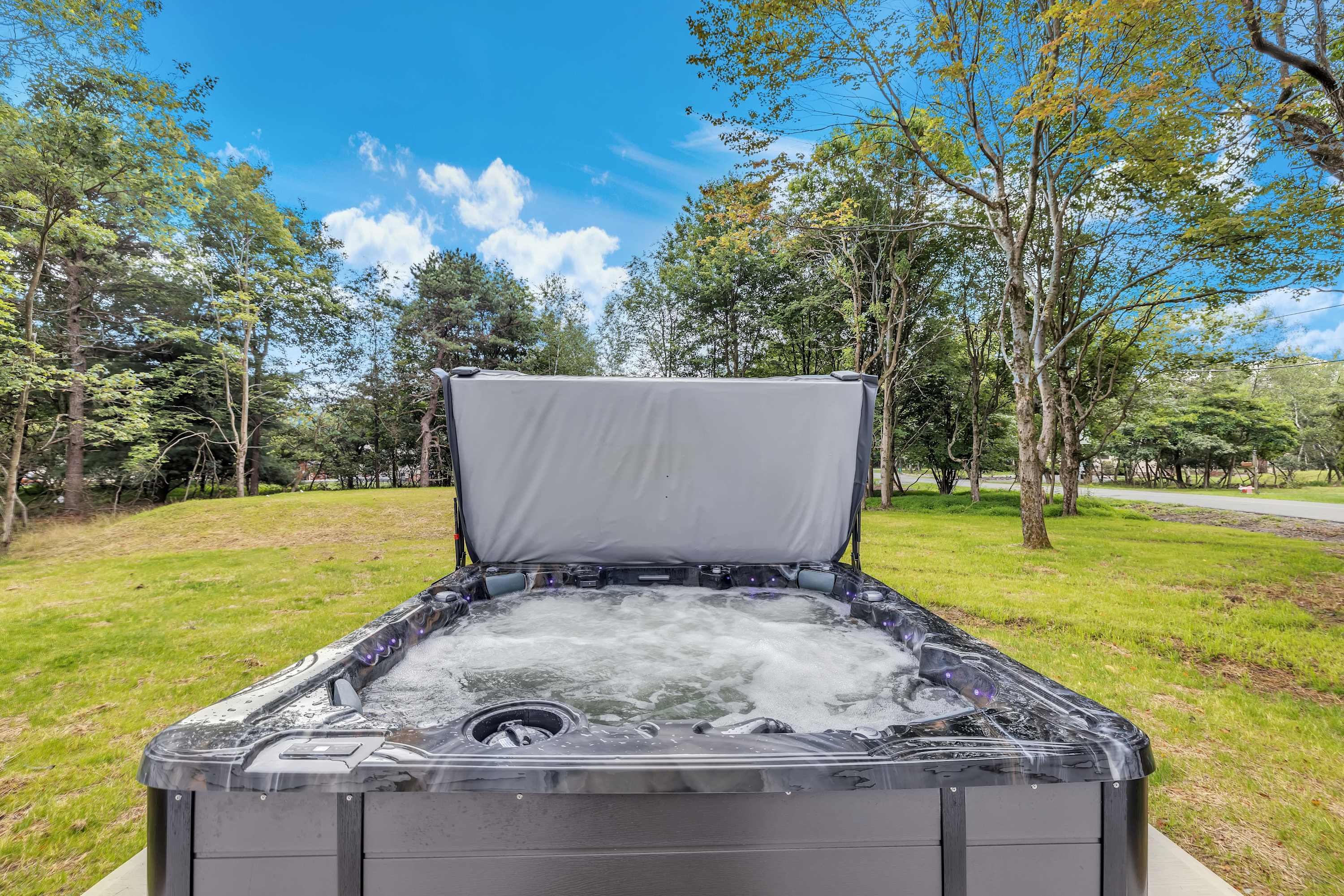 Relax in the Hot Tub – A spacious, bubbling hot tub set against a lush green backdrop, perfect for unwinding in complete privacy.