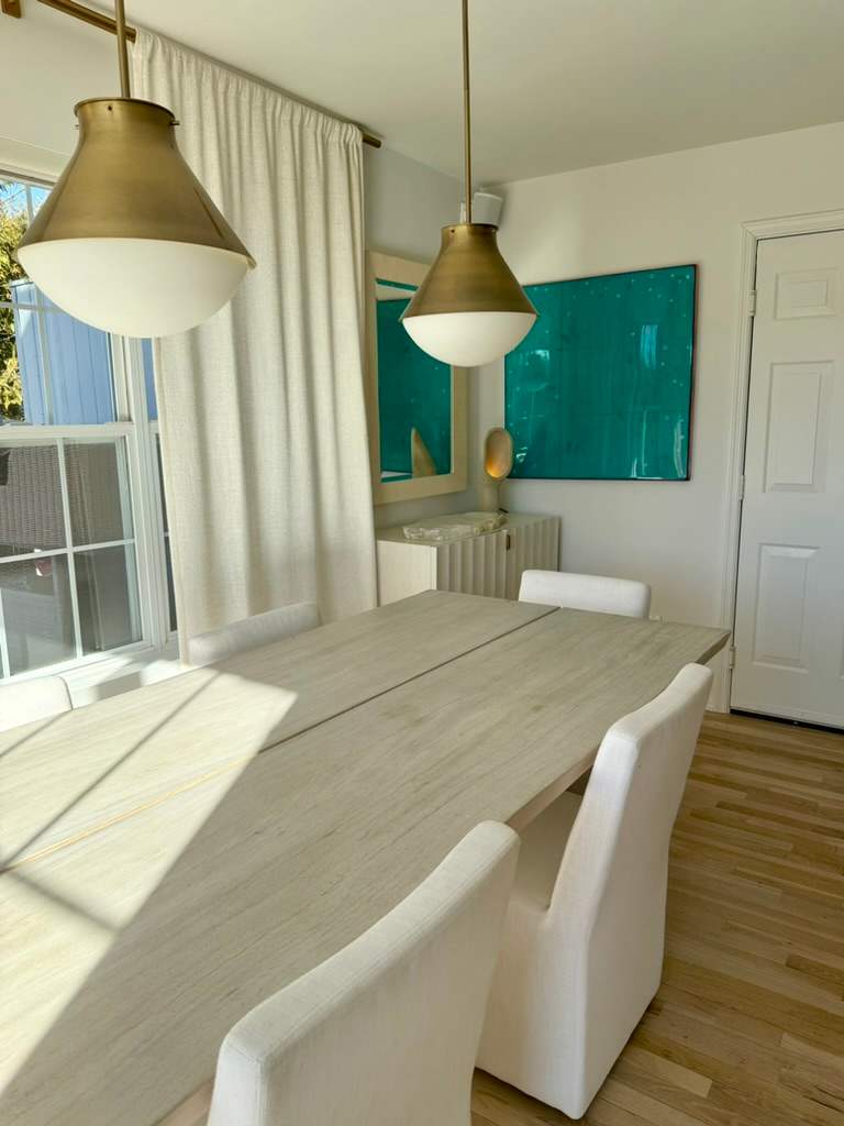 Dining table with upholstered chairs beneath a pair of brass pendant lights.
