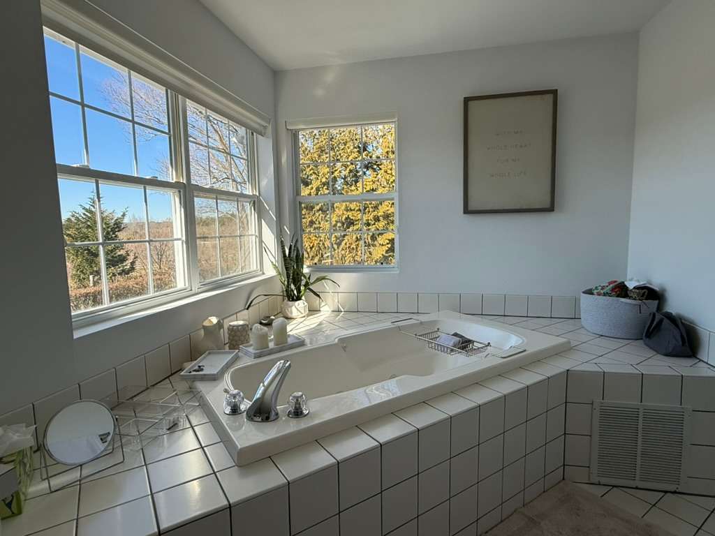 Bathroom with a tiled jetted soaking tub beneath a garden-view window.
