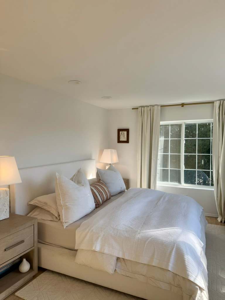Bedroom with a queen bed, white linens, and a window seat nook.