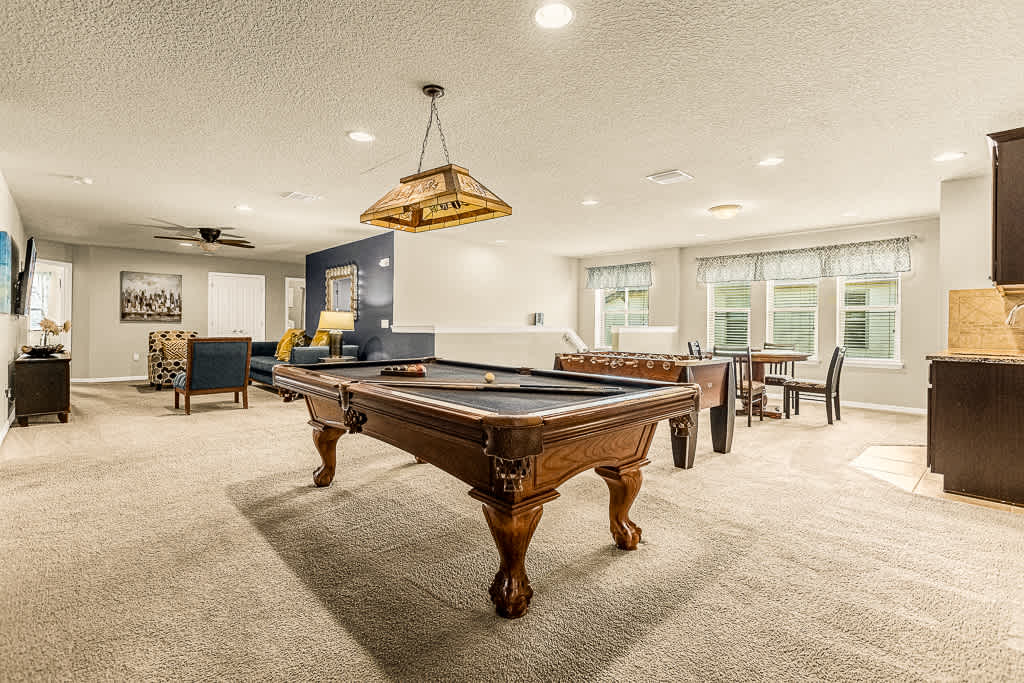 Spacious game room with pool and foosball tables, perfect for entertaining and relaxation. Enjoy natural light and ample seating for fun gatherings!
