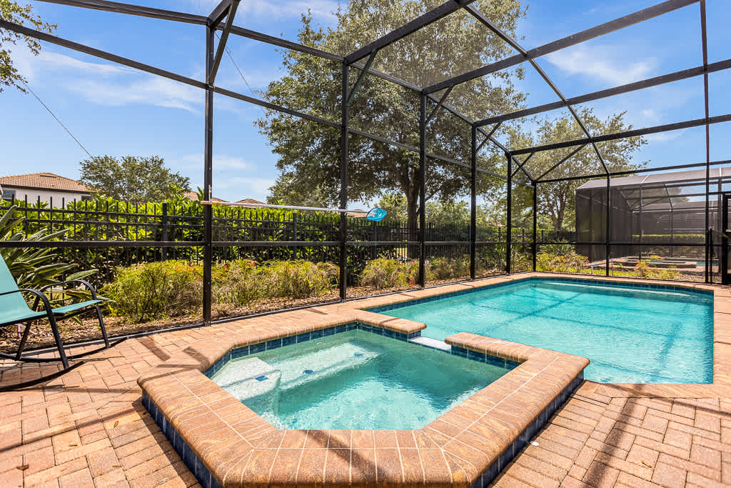 Relax in your private screened pool and hot tub oasis, surrounded by lush greenery and perfect for sunny days.