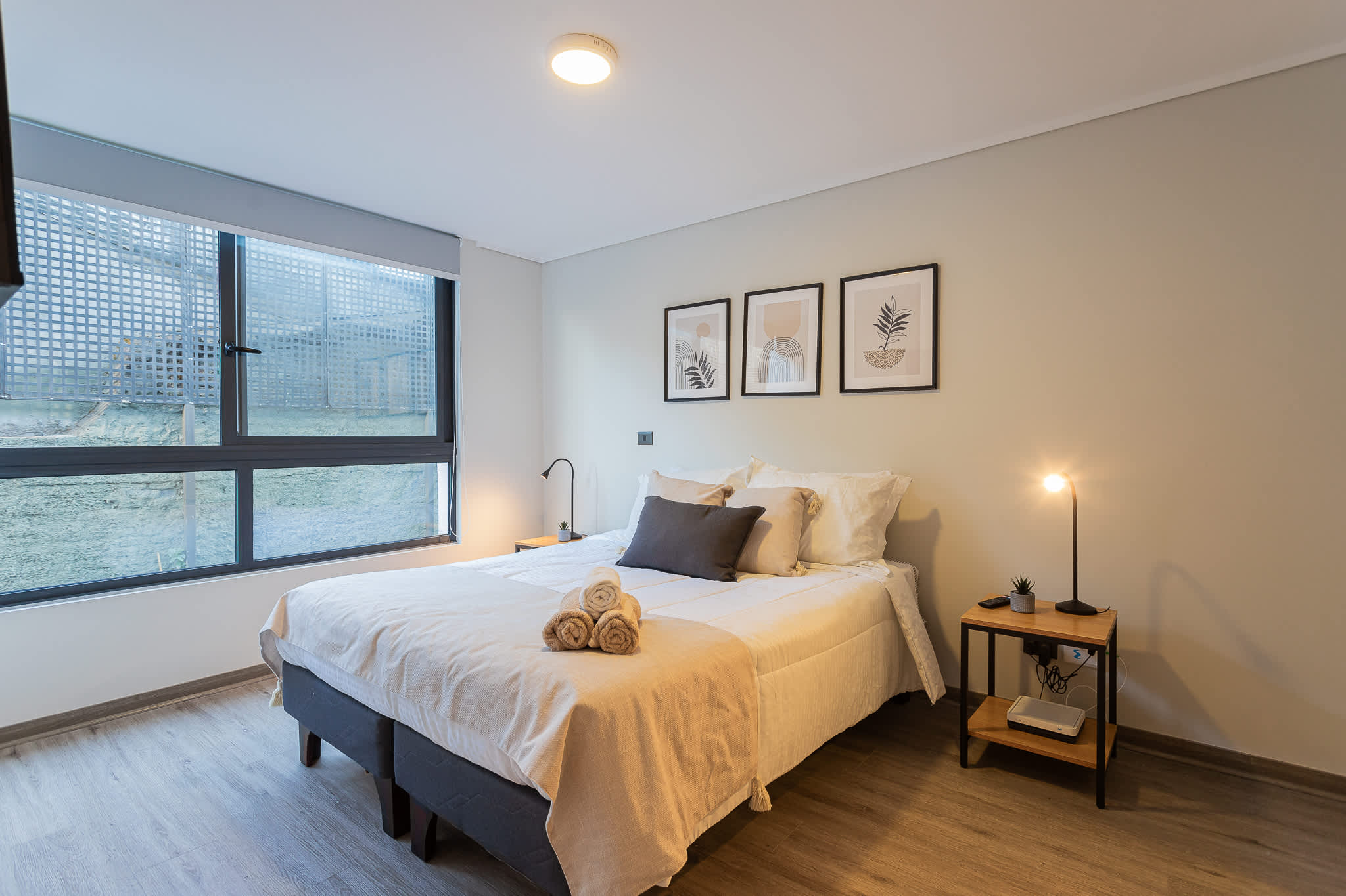 Relax in this serene bedroom with modern decor and ample natural light, perfect for unwinding after a day exploring the city.