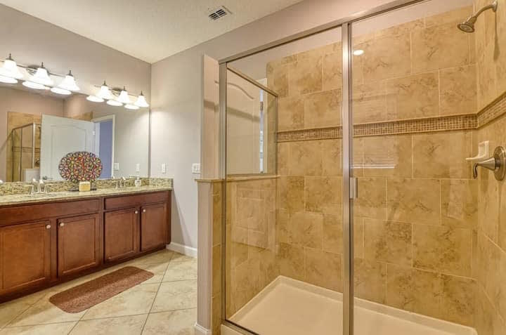 Spa-style bathroom w/ glass shower and warm stone finishes.