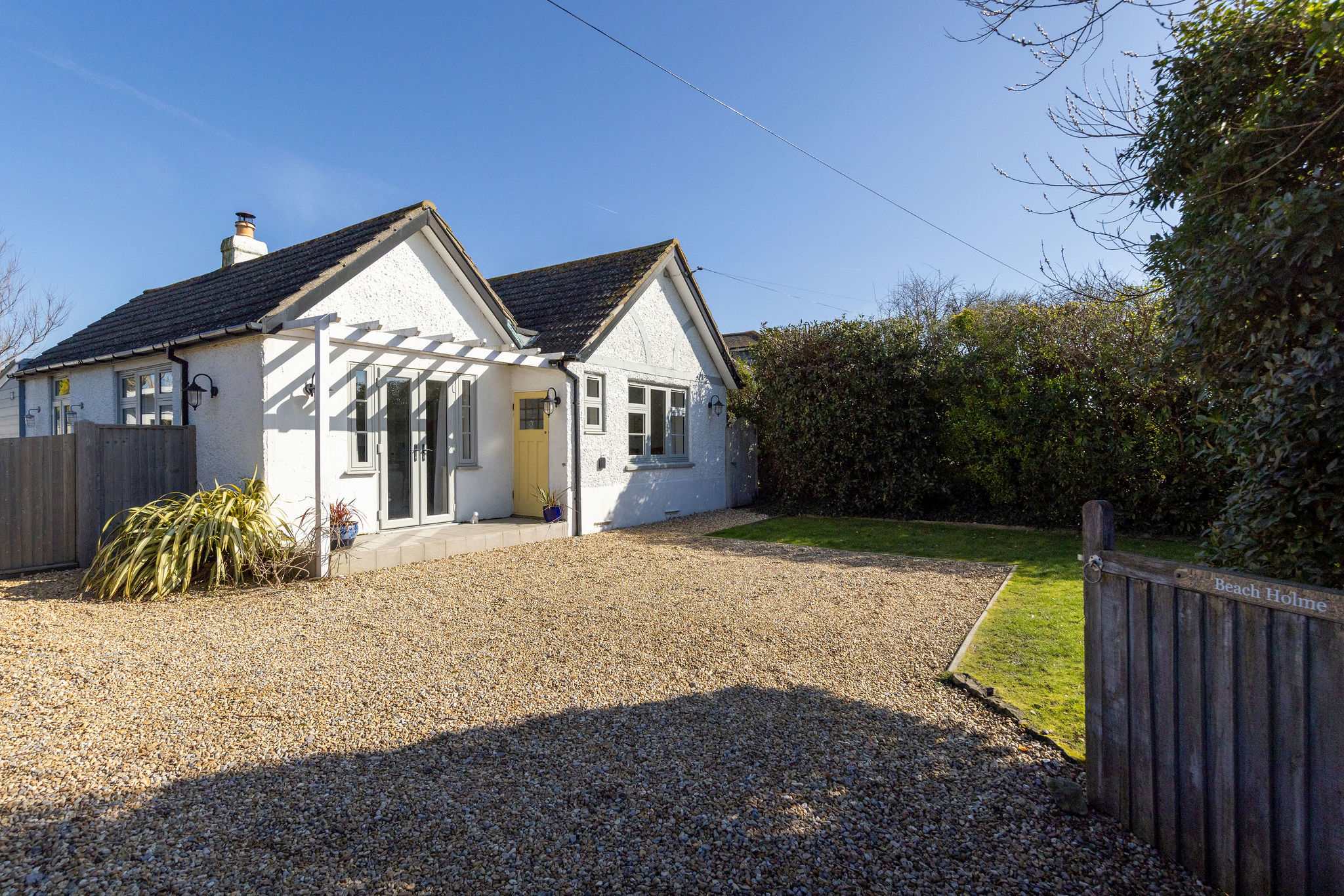 Beach Holme, showcases its inviting white exterior, pitched roofs, and a welcoming large gravel driveway to park multiple cars.