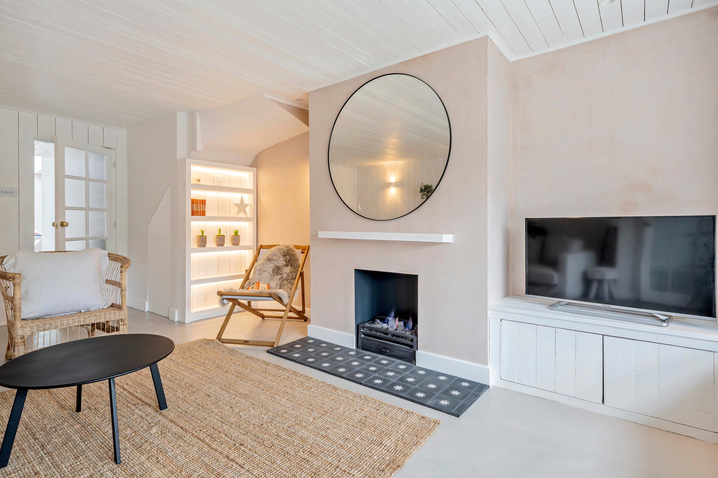 A contemporary living room showcasing a built-in fireplace beneath a large round mirror.