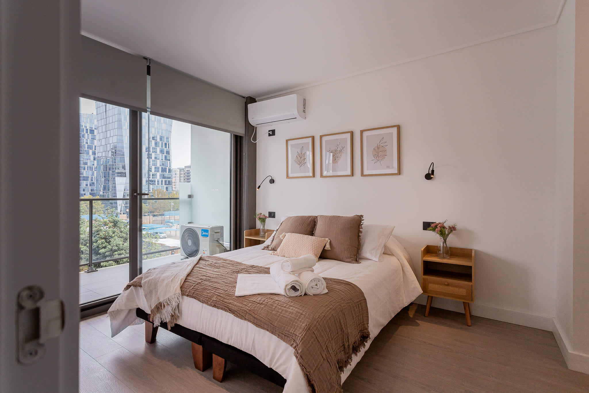 Relax in this modern bedroom with city views, featuring cozy decor and a touch of nature for your perfect getaway.