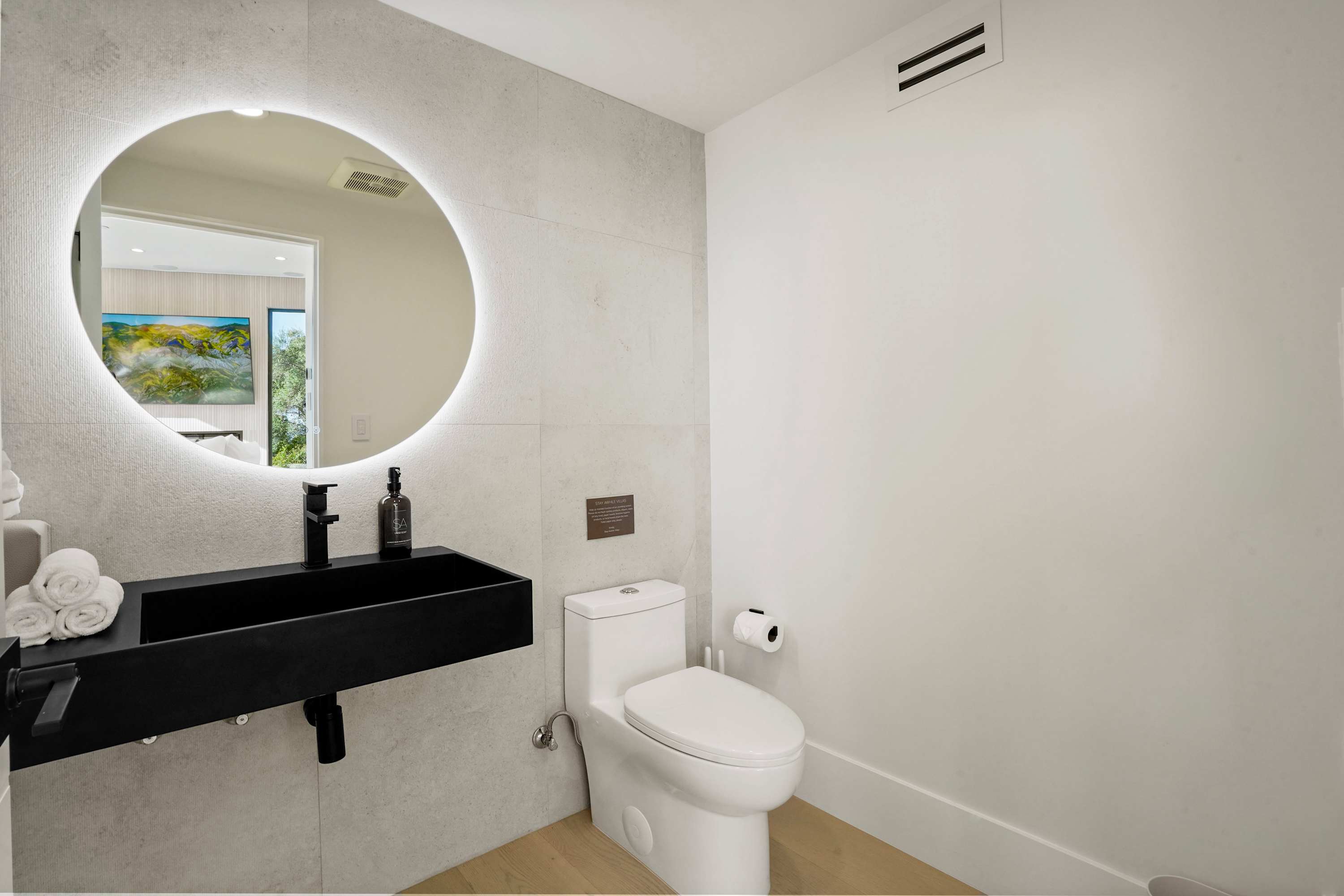 Powder bathroom with floating vanity, circular mirror, and matte black fixtures.