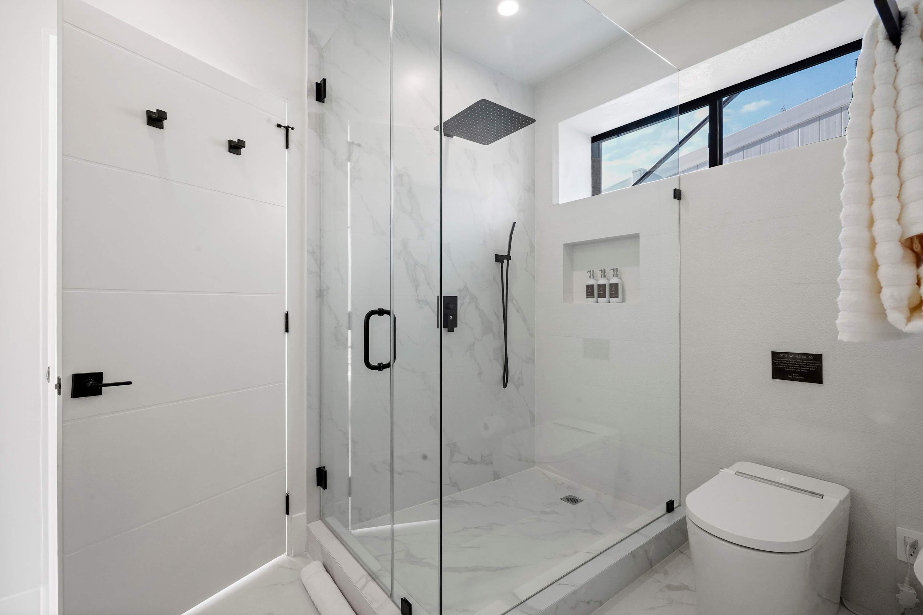 Walk-in glass shower with built-in bench, handheld showerhead, and matte black fittings.