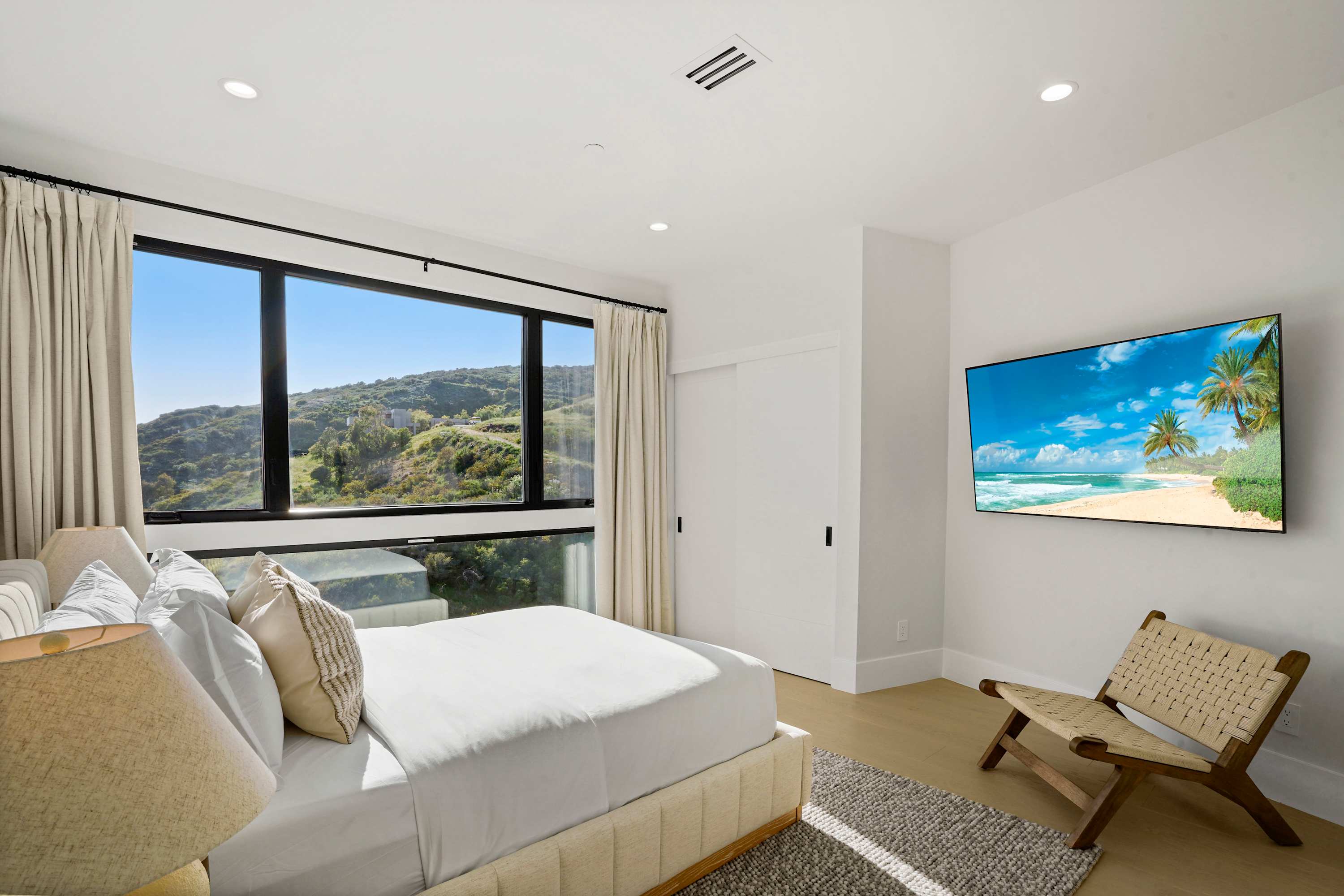 Guest bedroom with king bed, lounge chair, Smart TV, and panoramic hillside views.