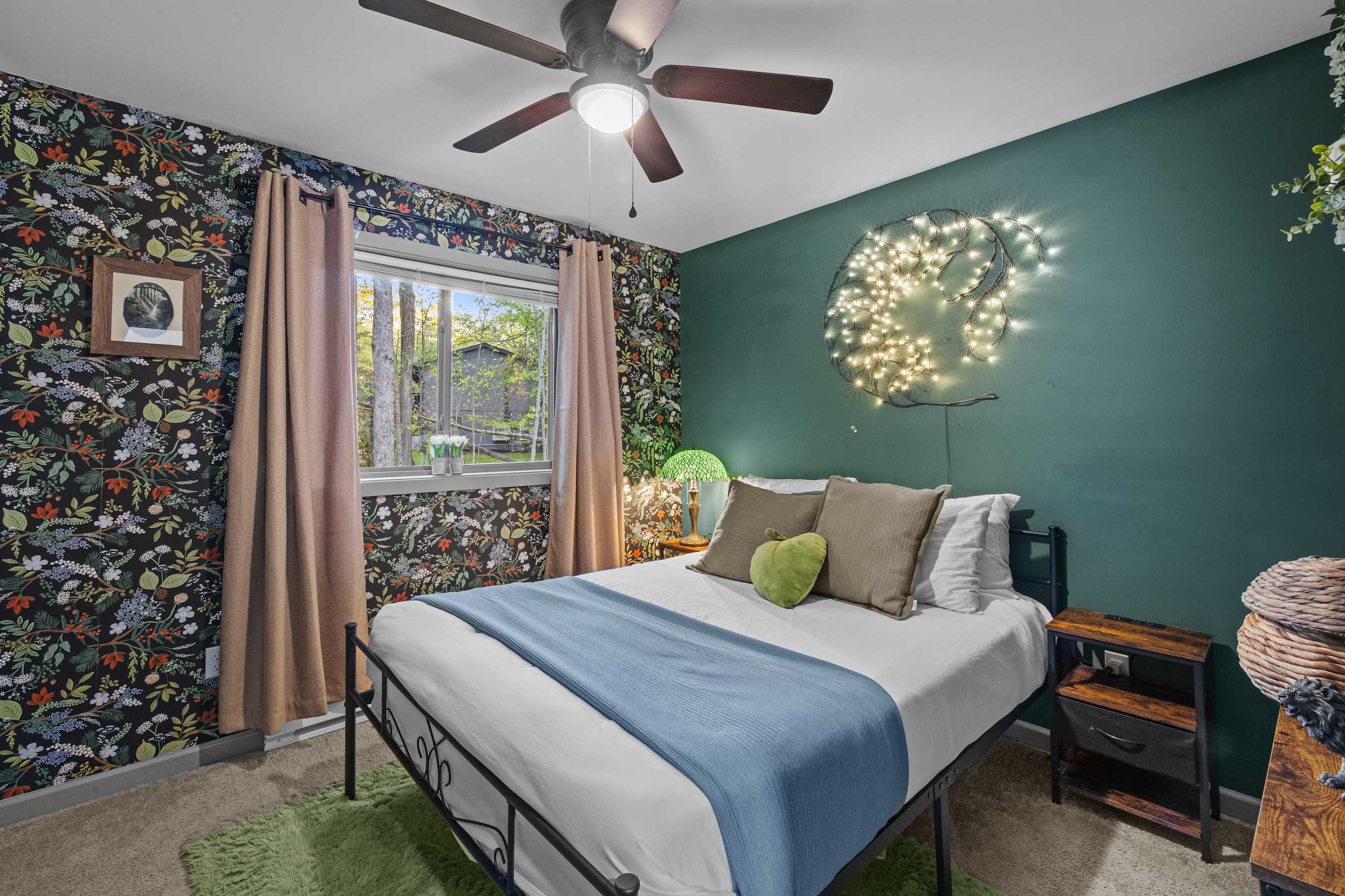 Sleep like you're in a dream! This stylish bedroom with tree-inspired wall decor and floral wallpaper is the perfect mix of charm and comfort. Enjoy the peaceful vibe with room darkening shades and a ceiling fan for a cool, restful night.