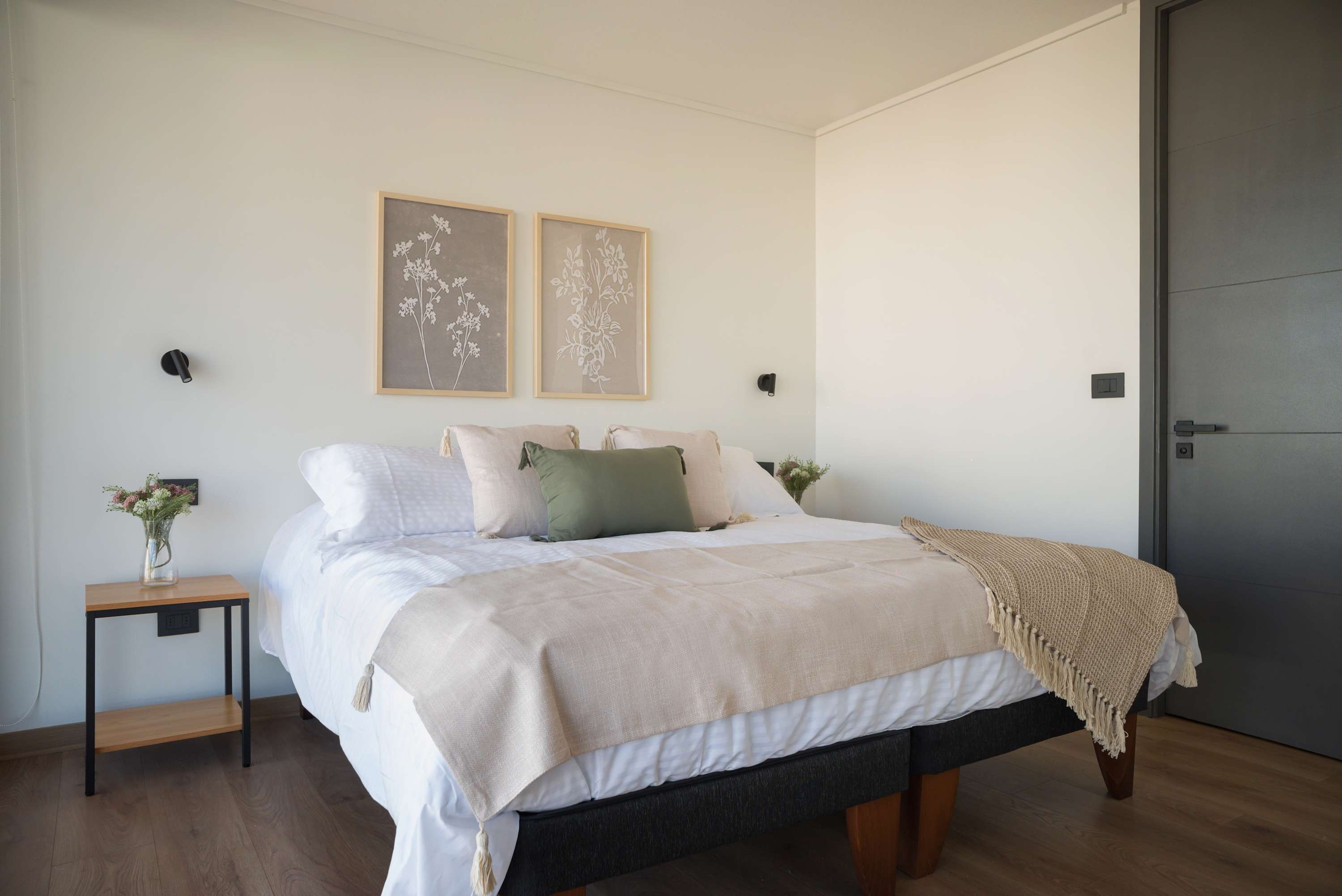 Relax in this serene bedroom featuring cozy linens, botanical art, and natural light—perfect for unwinding after a day exploring the city.