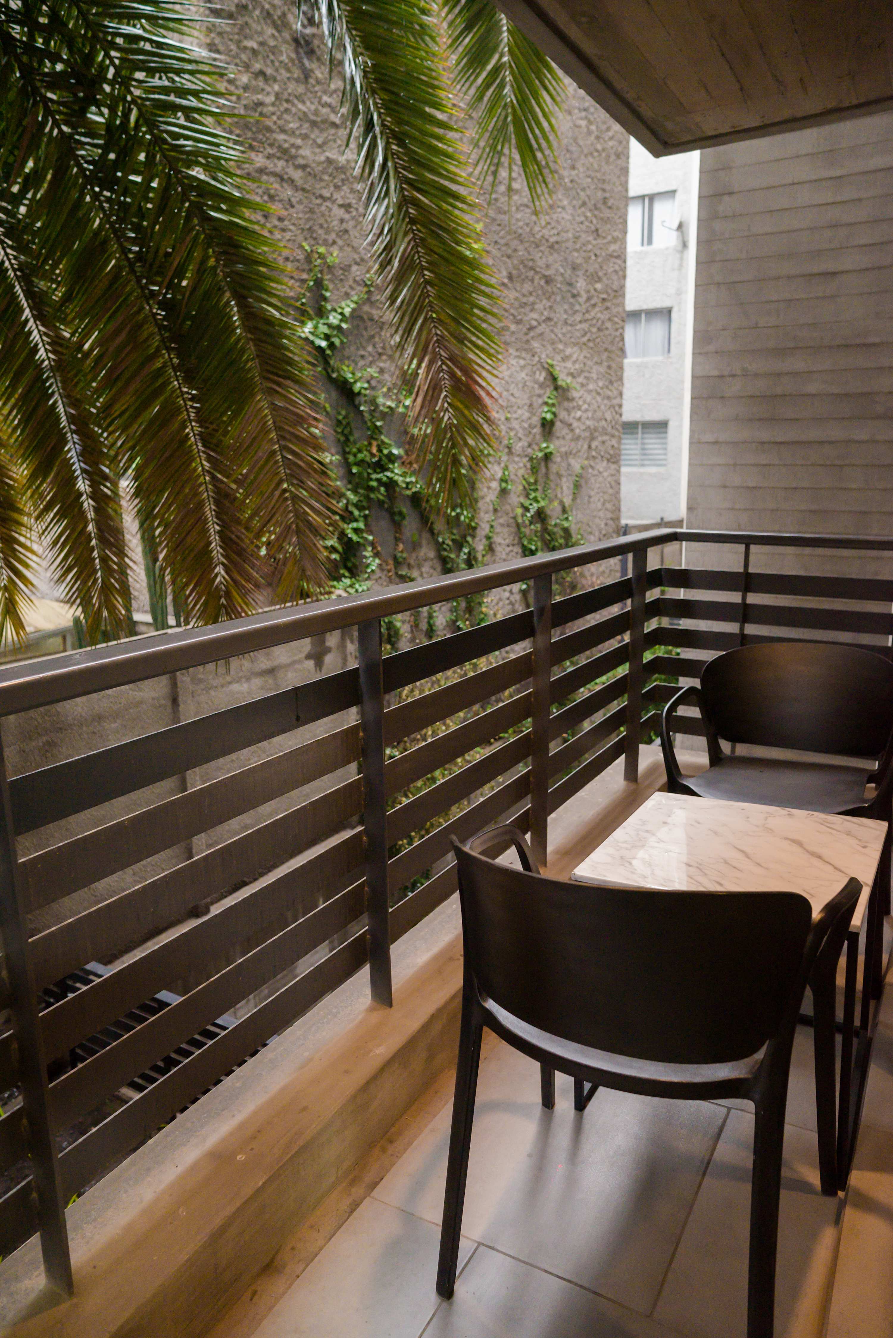 Relax on your private balcony with lush greenery and a cozy seating area, perfect for morning coffee or evening relaxation.