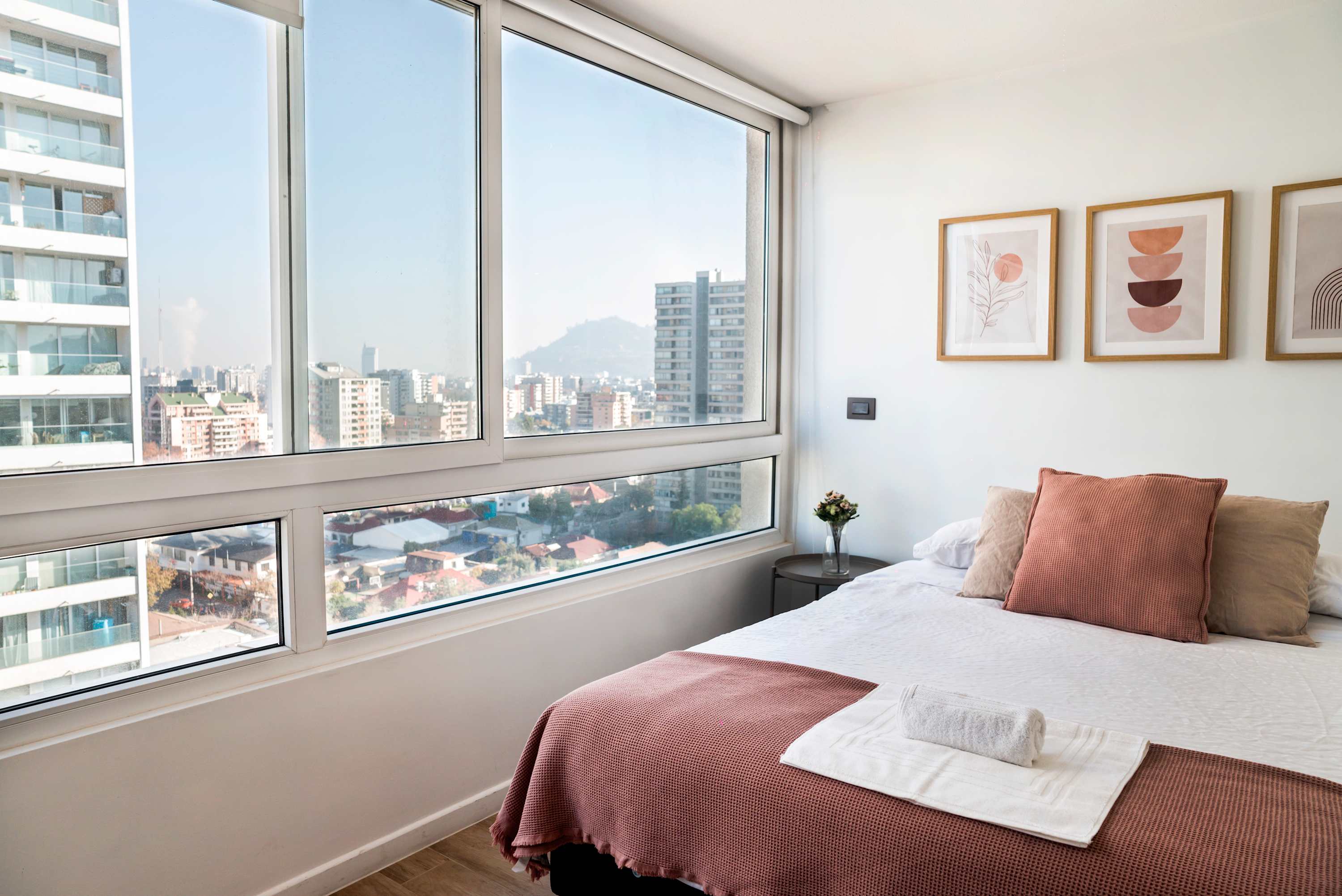 Enjoy breathtaking city views from this modern, cozy bedroom with stylish decor and plush bedding.